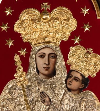 Zdjęcie nr 3: Obraz Matki Boskiej z Dzieciątkiem w kształcie stojącego prostokąta zamkniętego łukiem nadwieszonym. W centrum przedstawiona została Maria, trzymająca na lewej ręce Dzieciątko Jezus, z berłem w prawej. Maria spogląda na widza, ma owalną twarz o dużych, brązowych oczach, wąskim nosie i niewielkich, kształtnych ustach. Dzieciątko patrzy przed siebie, prawą ręką czyni gest błogosławieństwa, lewą trzyma rękę Marii. Poza widocznymi twarzami, rękami oraz stopami Dzieciątka resztę postaci zakrywają srebrne sukienki i złocone korony. Postacie zostały umieszczone na tle wykonanym z czerwonej tkaniny. Sukienki pokrywa gęsty wzór liściasto-kwiatowy złożony z rozwiniętych kwiatów i bujnych, mięsistych liści, z szerokim lamowaniem zdobionym rombowymi kaboszonami i krzyżykami. Dolna partia jest nowsza, dosztukowana i pokryta podobnym, choć rzadszym wzorem. Korony są złocone, wysokie, wypukłe, częściowo puklowane i trybowane w ornament z bujnej wici akantowej, nad czołem zdobione szlakiem z kaboszonów, a u  góry perełkowaniem i zwieńczone kulą z krzyżem. Wokół głowy Marii dodatkowo 12 gwiazdek. Matka Boska w prawej dłoni trzyma berło o rękojeści zdobionej dołem liśćmi akantu, a u góry rombowymi kaboszonami. 