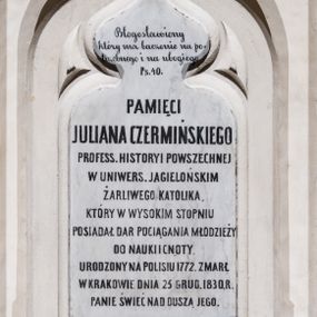 Zdjęcie nr 1: Epitafium w kształcie stojącego prostokąta zamkniętego łukiem w ośli grzbiet z krzyżem, wsparte na konsoli wpisanej w formę trójkąta zwróconego ku dołowi, o bokach profilowanych, lekko wklęsłych, z tarczą herbową. W polu tarczy nakrytej hełmem z koroną otwartą i klejnotem w postaci strusich piór znajduje się godło herbu Ramułt – pięć róż. W część środkową wpisany maswerk, w jego polu inskrypcja „Błogosławiony / który ma baczenie na po/trzebnego i na ubogiego / Ps. 40. / PAMIĘCI / JULIANA CZERMIŃSKIEGO / PROFESS(ORA) HISTORYI POWSZECHNEJ / W UNIWERS(YTECIE) JAGIELOŃSKIM / ŻARLIWEGO KATOLIKA, / KTÓRY W WYSOKIM STOPNIU / POSIADAŁ DAR POCIĄGANIA MŁODZIEŻY / DO NAUKI I CNOTY. / URODZONY NA POLISIU 1772. ZMARŁ / W KRAKOWIE DNIA 25 GRUD(NIA) 1830. R(OKU) / PANIE ŚWIEĆ NAD DUSZĄ JEGO.”
