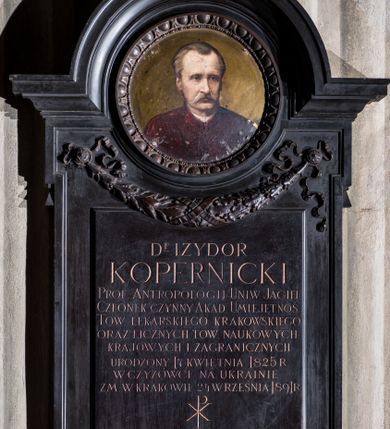 Zdjęcie nr 1: Epitafium w kształcie stojącego prostokąta, z uszakami, zwieńczonego profilowanym gzymsem o wykroju łuku nadwieszonego. Pod górnymi i dolnymi uszakami łezki. W górnej części okrągłe pole z portretem zmarłego na miedzianej blasze obwiedzione dekoracją z wolich oczu i sznura. Pod portretem feston utworzony z liści lauru i dębu, podwieszony na dwóch rozetach z karbowanymi, wijącymi się taśmami. Na portrecie widoczny mężczyzna w ujęciu popiersiowym, z głową zwróconą lekko w lewo, ubrany w bordową togę. Jego twarz jest pociągła, oczy szeroko otwarte, nos długi, wargi częściowo zasłonięte wąsami, brązowe włosy zaczesane do tyłu odsłaniające zakola; tło nieokreślone, w jasnobrązowej tonacji kolorystycznej. W polu poniżej portretu inskrypcja „D(OKTO)R IZYDOR / KOPERNICKI / PROF(ESOR) ANTROPOLOGII UNIW(ERSYTETU) JAGIEL(LOŃSKIEGO) / CZŁONEK CZYNNY AKAD(EMII) UMIEJĘTNOŚ(CI) / TOW(ARZYSTWA) LEKARSKIEGO KRAKOWSKIEGO / ORAZ LICZNYCH TOW(ARZYSTW) NAUKOWYCH / KRAJOWYCH I ZAGRANICZNYCH / URODZONY 17 KWIETNIA 1825 R(OKU) W CZYŻÓWCE NA UKRAINIE / ZM(ARŁY) W KRAKOWIE 24 WRZEŚNIA 1891 R(OKU) / CZŁONKOWIE AKAD(EMII) UMIEJ(ĘTNOŚCI) – WYDZIAŁ / LEKARSKI UNIW(ERSYTETU) JAG(IELLOŃSKIEGO) – TOWARZYSTWO / LEKARSKIE KRAKOWSKIE / PRZEKAZUJĄ WDZIĘCZNEJ PAMIĘCI / POTOMNYCH NIESKAZITELNE IMIĘ / ZASŁUŻONEGO OBYWATELA / I GŁOŚNEJ SŁAWY UCZONEGO.”. 