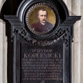 Zdjęcie nr 1: Epitafium w kształcie stojącego prostokąta, z uszakami, zwieńczonego profilowanym gzymsem o wykroju łuku nadwieszonego. Pod górnymi i dolnymi uszakami łezki. W górnej części okrągłe pole z portretem zmarłego na miedzianej blasze obwiedzione dekoracją z wolich oczu i sznura. Pod portretem feston utworzony z liści lauru i dębu, podwieszony na dwóch rozetach z karbowanymi, wijącymi się taśmami. Na portrecie widoczny mężczyzna w ujęciu popiersiowym, z głową zwróconą lekko w lewo, ubrany w bordową togę. Jego twarz jest pociągła, oczy szeroko otwarte, nos długi, wargi częściowo zasłonięte wąsami, brązowe włosy zaczesane do tyłu odsłaniające zakola; tło nieokreślone, w jasnobrązowej tonacji kolorystycznej. W polu poniżej portretu inskrypcja „D(OKTO)R IZYDOR / KOPERNICKI / PROF(ESOR) ANTROPOLOGII UNIW(ERSYTETU) JAGIEL(LOŃSKIEGO) / CZŁONEK CZYNNY AKAD(EMII) UMIEJĘTNOŚ(CI) / TOW(ARZYSTWA) LEKARSKIEGO KRAKOWSKIEGO / ORAZ LICZNYCH TOW(ARZYSTW) NAUKOWYCH / KRAJOWYCH I ZAGRANICZNYCH / URODZONY 17 KWIETNIA 1825 R(OKU) W CZYŻÓWCE NA UKRAINIE / ZM(ARŁY) W KRAKOWIE 24 WRZEŚNIA 1891 R(OKU) / CZŁONKOWIE AKAD(EMII) UMIEJ(ĘTNOŚCI) – WYDZIAŁ / LEKARSKI UNIW(ERSYTETU) JAG(IELLOŃSKIEGO) – TOWARZYSTWO / LEKARSKIE KRAKOWSKIE / PRZEKAZUJĄ WDZIĘCZNEJ PAMIĘCI / POTOMNYCH NIESKAZITELNE IMIĘ / ZASŁUŻONEGO OBYWATELA / I GŁOŚNEJ SŁAWY UCZONEGO.”. 