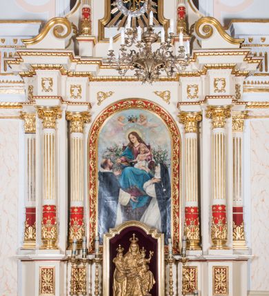 Zdjęcie nr 2: Ołtarz architektoniczny, jednokondygnacyjny, jednoosiowy, ze zwieńczeniem. Prostopadłościenny ołtarz, z antepedium artykułowanym 3 płycinami o dekoracyjnym wykroju, wtopiony jest z dolną partią, zryzalitowanego cokołu retabulum, której układ powtarza także górna partia cokołu. Część środkowa ujęta jest trzema parami kolumn korynckich, z których środkowe są wysunięte i ustawione na tle filarów. Podpory wspierają wyłamujące się ponad nimi, przerwane w partii architrawu i fryzu belkowanie. Druga kondygnacja jest w formie stojącego prostokąta ujętego parą ustawionych na cokołach kolumienek wspierających przerwane, wyłamujące się ponad nimi belkowanie. Dodatkowo ujmuje ją para spływów wolutowych oraz przerwany, wolutowy przyczółek. Zwieńczenie zamknięte jest parą stykających się wolut oraz ujęte przerwanym przyczółkiem wolutowym. Szczyt jest w formie ażurowej ornamentyki akantowo-rocaille’owej. W polu środkowym retabulum jest obraz w kształcie stojącego prostokąta zamkniętego półkoliście z przedstawieniem Matki Boskiej Różańcowej ze św. Dominikiem i św. Małgorzatą Alacoque. W polu zwieńczenia profilowana rama w kształcie prostokąta z uszakami w narożach, zamkniętego łukiem odcinkowym, z ażurowym monogramem maryjnym pośrodku, ujętym wieńcem obłoków i promienistą glorią. Retabulum zdobi stylizowana ornamentyka roślinna w postaci liści akantu i  dziewięćsiłu w formie rozet w płycinach antepedium i górnej partii cokołu retabulum oraz we fryzie. Nasada trzonów kolumn ujęta liśćmi akantu i gałązkami róż. Gzyms belkowania zdobi motyw astragalu. Struktura ołtarza utrzymana jest odcieniu kremowym, detal architektoniczny i ornamentyka częściowo są polichromowane w kolorze czerwonym oraz złocone.  