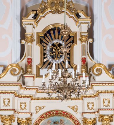 Zdjęcie nr 4: Ołtarz architektoniczny, jednokondygnacyjny, jednoosiowy, ze zwieńczeniem. Prostopadłościenny ołtarz, z antepedium artykułowanym 3 płycinami o dekoracyjnym wykroju, wtopiony jest z dolną partią, zryzalitowanego cokołu retabulum, której układ powtarza także górna partia cokołu. Część środkowa ujęta jest trzema parami kolumn korynckich, z których środkowe są wysunięte i ustawione na tle filarów. Podpory wspierają wyłamujące się ponad nimi, przerwane w partii architrawu i fryzu belkowanie. Druga kondygnacja jest w formie stojącego prostokąta ujętego parą ustawionych na cokołach kolumienek wspierających przerwane, wyłamujące się ponad nimi belkowanie. Dodatkowo ujmuje ją para spływów wolutowych oraz przerwany, wolutowy przyczółek. Zwieńczenie zamknięte jest parą stykających się wolut oraz ujęte przerwanym przyczółkiem wolutowym. Szczyt jest w formie ażurowej ornamentyki akantowo-rocaille’owej. W polu środkowym retabulum jest obraz w kształcie stojącego prostokąta zamkniętego półkoliście z przedstawieniem Matki Boskiej Różańcowej ze św. Dominikiem i św. Małgorzatą Alacoque. W polu zwieńczenia profilowana rama w kształcie prostokąta z uszakami w narożach, zamkniętego łukiem odcinkowym, z ażurowym monogramem maryjnym pośrodku, ujętym wieńcem obłoków i promienistą glorią. Retabulum zdobi stylizowana ornamentyka roślinna w postaci liści akantu i  dziewięćsiłu w formie rozet w płycinach antepedium i górnej partii cokołu retabulum oraz we fryzie. Nasada trzonów kolumn ujęta liśćmi akantu i gałązkami róż. Gzyms belkowania zdobi motyw astragalu. Struktura ołtarza utrzymana jest odcieniu kremowym, detal architektoniczny i ornamentyka częściowo są polichromowane w kolorze czerwonym oraz złocone.  