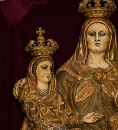 Zdjęcie nr 4: Płaskorzeźba przedstawia całopostaciowy wizerunek św. Anny Samotrzeć. Ukazana w pozycji siedzącej święta zwrócona jest w trzech czwartych w prawo, z głową skierowaną na wprost. Owalną twarz charakteryzują wyraziste, surowe rysy dojrzałej kobiety. Strój św. Anny składa się z sukni, osłaniającego nogi płaszcza zdobionego stylizowaną ornamentyką roślinną oraz osłaniającej głowę chusty związanej na piersiach. Na stopach są sandały. Święta lewą ręką podtrzymuje siedzące na jej kolanach Dzieciątko Jezus zwrócone w trzech czwartych w prawo. Zaokrągloną twarz charakteryzują pełne, dziecięce rysy, włosy są krótkie skręcone. Jezus ubrany jest w długą, przewiązaną w pasie suknię z podwiniętymi rękawami. Prawą rękę wspiera na piersiach, lewą unosi, trzymając w dłoni gałązkę różaną. Po lewej stronie, obok św. Anny stoi Maria ukazana jako kilkunastoletnia dziewczyna. Święta Anna wspiera prawą rękę na prawym ramieniu córki. Maria zwrócona jest w trzech czwartych w lewo. Owalną twarz charakteryzują młodzieńcze rysy. Ubrana jest w zdobioną ornamentem roślinnym suknię oraz osłaniający nogi, podpięty w pasie płaszcz. Na głowę ma nałożoną opadającą na ramiona chustę, odsłaniającą częściowo włosy. Maria wyciąga ręce w kierunku Dzieciątka Jezus. Na głowach postaci znajdują się zamknięte korony. Odsłonięte partie ciała utrzymane są w bladym odcieniu karnacji. Ubiór oraz atrybuty są złocone. Płaskorzeźba umieszczona jest w płytkiej niszy w kształcie stojącego prostokąta zamkniętego uskokowym łukiem nadwieszonym, wyłożonej bordowym aksamitem oraz ujętej profilowaną, złoconą ramą.    