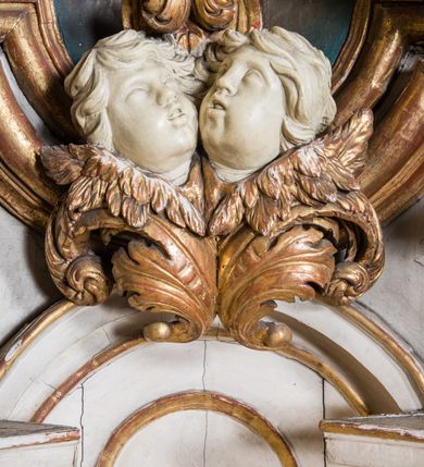 Zdjęcie nr 8: Ołtarz architektoniczny, jednokondygnacyjny, jednoosiowy, ze zwieńczeniem. Ołtarz prostopadłościenny, murowany. Retabulum o strukturze wklęsłej wzdłuż osi pionowej osadzone na niewysokim, cokole zryzalitowanym w formie pary impostów. Gzyms cokołu pośrodku ma formę półkolistego łuku nadwieszonego. Część środkowa ujęta parą wąskich filarów, licami zwróconych ukośnie na zewnątrz, wspierających wydatny gzyms osadzony na parze spływów wolutowych. Pola cokołu retabulum zdobione ornamentyką roślinną. Na impostach para figur aniołków, stojący po lewej stronie w lewej dłoni ma zwój z napisem „PATRZ / SWEGO / A NIE / PRAGNIJ / CUDZEGO”, stojący po prawej trzyma lewą ręką wspartą na podłożu tarczę z napisem „ZLE / NABYTE / NIE / BĘDZIE / DOBRZE / SPOŻYTE”. Między impostami płycina w kształcie prostokąta leżącego o wklęsłych górnych narożach i zamkniętego półkolistym łukiem nadwieszonym. W dolnej partii retabulum para uskrzydlonych główek anielskich dołem ujętych liśćmi akantu. Lica filarów zdobione motywem kampanuli. W partii belkowania, pośrodku motyw akantowego kartusza z napisem „VENI / CORONABE/RIS.”, ujętego górą, dołem i po bokach motywami uskrzydlonych główek anielskich. Zwieńczenie w formie promienistej glorii z koroną osadzoną na obłokach. Całość flankuje para siedzących na gzymsie aniołów w dynamicznych pozach. Pole części środkowej w kształcie stojącego prostokąta ujętego górą i dołem parą zwróconych do siebie półkolistych łuków nadwieszonych z uskokami, ujęte profilowaną, złoconą ramą. Wewnątrz obraz z wizerunkiem Matki Boskiej. Struktura polichromowana w kolorze białym, detal architektoniczny i ornamentyka złocone i srebrzone.