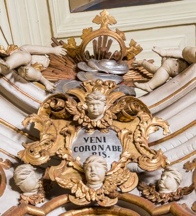 Zdjęcie nr 5: Ołtarz architektoniczny, jednokondygnacyjny, jednoosiowy, ze zwieńczeniem. Ołtarz prostopadłościenny, murowany. Retabulum o strukturze wklęsłej wzdłuż osi pionowej osadzone na niewysokim, cokole zryzalitowanym w formie pary impostów. Gzyms cokołu pośrodku ma formę półkolistego łuku nadwieszonego. Część środkowa ujęta parą wąskich filarów, licami zwróconych ukośnie na zewnątrz, wspierających wydatny gzyms osadzony na parze spływów wolutowych. Pola cokołu retabulum zdobione ornamentyką roślinną. Na impostach para figur aniołków, stojący po lewej stronie w lewej dłoni ma zwój z napisem „PATRZ / SWEGO / A NIE / PRAGNIJ / CUDZEGO”, stojący po prawej trzyma lewą ręką wspartą na podłożu tarczę z napisem „ZLE / NABYTE / NIE / BĘDZIE / DOBRZE / SPOŻYTE”. Między impostami płycina w kształcie prostokąta leżącego o wklęsłych górnych narożach i zamkniętego półkolistym łukiem nadwieszonym. W dolnej partii retabulum para uskrzydlonych główek anielskich dołem ujętych liśćmi akantu. Lica filarów zdobione motywem kampanuli. W partii belkowania, pośrodku motyw akantowego kartusza z napisem „VENI / CORONABE/RIS.”, ujętego górą, dołem i po bokach motywami uskrzydlonych główek anielskich. Zwieńczenie w formie promienistej glorii z koroną osadzoną na obłokach. Całość flankuje para siedzących na gzymsie aniołów w dynamicznych pozach. Pole części środkowej w kształcie stojącego prostokąta ujętego górą i dołem parą zwróconych do siebie półkolistych łuków nadwieszonych z uskokami, ujęte profilowaną, złoconą ramą. Wewnątrz obraz z wizerunkiem Matki Boskiej. Struktura polichromowana w kolorze białym, detal architektoniczny i ornamentyka złocone i srebrzone.