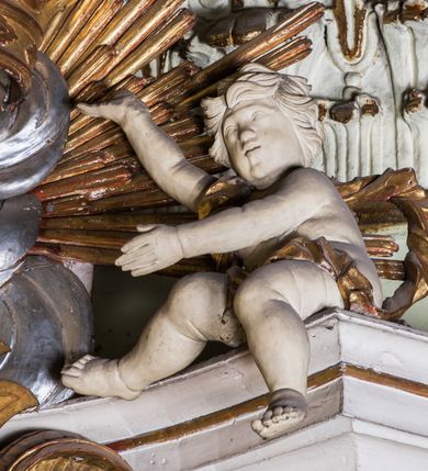 Zdjęcie nr 7: Ołtarz architektoniczny, jednokondygnacyjny, jednoosiowy, ze zwieńczeniem. Ołtarz prostopadłościenny, murowany. Retabulum o strukturze wklęsłej wzdłuż osi pionowej osadzone na niewysokim, cokole zryzalitowanym w formie pary impostów. Gzyms cokołu pośrodku ma formę półkolistego łuku nadwieszonego. Część środkowa ujęta parą wąskich filarów, licami zwróconych ukośnie na zewnątrz, wspierających wydatny gzyms osadzony na parze spływów wolutowych. Pola cokołu retabulum zdobione ornamentyką roślinną. Na impostach para figur aniołków, stojący po lewej stronie w lewej dłoni ma zwój z napisem „PATRZ / SWEGO / A NIE / PRAGNIJ / CUDZEGO”, stojący po prawej trzyma lewą ręką wspartą na podłożu tarczę z napisem „ZLE / NABYTE / NIE / BĘDZIE / DOBRZE / SPOŻYTE”. Między impostami płycina w kształcie prostokąta leżącego o wklęsłych górnych narożach i zamkniętego półkolistym łukiem nadwieszonym. W dolnej partii retabulum para uskrzydlonych główek anielskich dołem ujętych liśćmi akantu. Lica filarów zdobione motywem kampanuli. W partii belkowania, pośrodku motyw akantowego kartusza z napisem „VENI / CORONABE/RIS.”, ujętego górą, dołem i po bokach motywami uskrzydlonych główek anielskich. Zwieńczenie w formie promienistej glorii z koroną osadzoną na obłokach. Całość flankuje para siedzących na gzymsie aniołów w dynamicznych pozach. Pole części środkowej w kształcie stojącego prostokąta ujętego górą i dołem parą zwróconych do siebie półkolistych łuków nadwieszonych z uskokami, ujęte profilowaną, złoconą ramą. Wewnątrz obraz z wizerunkiem Matki Boskiej. Struktura polichromowana w kolorze białym, detal architektoniczny i ornamentyka złocone i srebrzone.