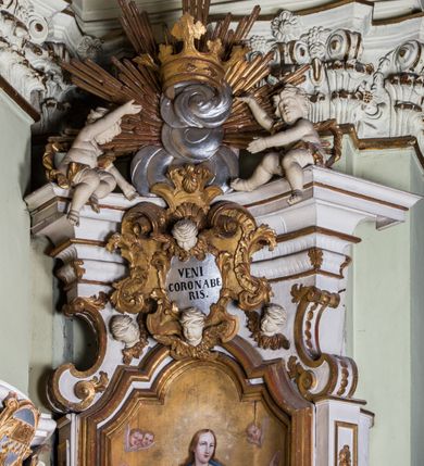 Zdjęcie nr 4: Ołtarz architektoniczny, jednokondygnacyjny, jednoosiowy, ze zwieńczeniem. Ołtarz prostopadłościenny, murowany. Retabulum o strukturze wklęsłej wzdłuż osi pionowej osadzone na niewysokim, cokole zryzalitowanym w formie pary impostów. Gzyms cokołu pośrodku ma formę półkolistego łuku nadwieszonego. Część środkowa ujęta parą wąskich filarów, licami zwróconych ukośnie na zewnątrz, wspierających wydatny gzyms osadzony na parze spływów wolutowych. Pola cokołu retabulum zdobione ornamentyką roślinną. Na impostach para figur aniołków, stojący po lewej stronie w lewej dłoni ma zwój z napisem „PATRZ / SWEGO / A NIE / PRAGNIJ / CUDZEGO”, stojący po prawej trzyma lewą ręką wspartą na podłożu tarczę z napisem „ZLE / NABYTE / NIE / BĘDZIE / DOBRZE / SPOŻYTE”. Między impostami płycina w kształcie prostokąta leżącego o wklęsłych górnych narożach i zamkniętego półkolistym łukiem nadwieszonym. W dolnej partii retabulum para uskrzydlonych główek anielskich dołem ujętych liśćmi akantu. Lica filarów zdobione motywem kampanuli. W partii belkowania, pośrodku motyw akantowego kartusza z napisem „VENI / CORONABE/RIS.”, ujętego górą, dołem i po bokach motywami uskrzydlonych główek anielskich. Zwieńczenie w formie promienistej glorii z koroną osadzoną na obłokach. Całość flankuje para siedzących na gzymsie aniołów w dynamicznych pozach. Pole części środkowej w kształcie stojącego prostokąta ujętego górą i dołem parą zwróconych do siebie półkolistych łuków nadwieszonych z uskokami, ujęte profilowaną, złoconą ramą. Wewnątrz obraz z wizerunkiem Matki Boskiej. Struktura polichromowana w kolorze białym, detal architektoniczny i ornamentyka złocone i srebrzone.
