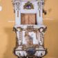 Zdjęcie nr 1: Ambona zawieszona jest na ścianie, z wejściem w zaplecku. Kosz ambony, na rzucie owalu, artykułują cztery pilastry osadzone na obiegającym jego podstawę cokole, wspierające wyłamujący się ponad nimi gzyms wieńczący. Podwieszenie kosza jest w formie czterech wolutowych kabłąków spiętych spłaszczonym pierścieniem. Zaplecek jest w formie prostokątnej płyciny ujętej parą pilastrów wspierających wyłamujące się ponad nimi belkowanie z wydatnym gzymsem. Zwieńczenie ma formę półkolistego przyczółka. Pola kosza ambony wypełniają płaskorzeźbione przedstawienia trzech świętych Janów. W środkowym znajduje się św. Jan Kanty siedzący przy pulpicie z otwartą księgą, poniżej znajduje się

kartusz herbowy, o krawędziach zdobionych ornamentyką akantową, z napisem: „Et lex / clementia / in linqua / eius”, natomiast w medalionie powyżej jest zamknięta księga z siedmioma pieczęciami. Po lewej znajduje się św. Jan Ewangelista, poniżej na kartuszu napis: „Quia verum est testimo/nium eius”, w medalionie zaś klatka. Po prawej jest przedstawienie św. Jana Chrzciciela z kartuszem z napisem: „Et enim / manus Domini / errat /cum / suo” oraz medalionem ze znakiem ręki trzymającej trąbę. Pilastry zdobią motywy kampanulli oraz uskrzydlonych główek anielskich, z których niektóre są na tle konch. Tuż pod gzymsem wieńczącym podwieszona jest girlanda kwiatowa. Belkowanie zaplecka ambony wsparte jest dodatkowo na wolutowych wspornikach, trzony pilastrów zdobią kampanulle. Po środku płyciny zaplecka, nad wejściem znajduje się ujęty akantem kartusz herbowy z napisem: „Docebit vos omnia”. Zwieńczenie ambony zdobią figurki dwóch par aniołków, z czego jedna usytuowana jest na krawędziach przyczółka, druga wypełnia pole tympanonu. Ukazane naprzeciw siebie w pozycjach półleżących, o przeplatających się nogach obuczącz podtrzymują otwartą księgę z napisem: „EVANGELIUM IESU CHRISTI”. Szczyt zwieńczenia jest w formie promienistej glorii z gołębicą Ducha Świętego po środku. Struktura ambony jest pomalowana na biało, podobnie, jak odsłonięte partie ciał aniołków. Detal architektoniczny, ornamnetyka, szaty i skrzydła są złocone i srebrzone.