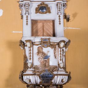 Zdjęcie nr 1: Ambona zawieszona jest na ścianie, z wejściem w zaplecku. Kosz ambony, na rzucie owalu, artykułują cztery pilastry osadzone na obiegającym jego podstawę cokole, wspierające wyłamujący się ponad nimi gzyms wieńczący. Podwieszenie kosza jest w formie czterech wolutowych kabłąków spiętych spłaszczonym pierścieniem. Zaplecek jest w formie prostokątnej płyciny ujętej parą pilastrów wspierających wyłamujące się ponad nimi belkowanie z wydatnym gzymsem. Zwieńczenie ma formę półkolistego przyczółka. Pola kosza ambony wypełniają płaskorzeźbione przedstawienia trzech świętych Janów. W środkowym znajduje się św. Jan Kanty siedzący przy pulpicie z otwartą księgą, poniżej znajduje się

kartusz herbowy, o krawędziach zdobionych ornamentyką akantową, z napisem: „Et lex / clementia / in linqua / eius”, natomiast w medalionie powyżej jest zamknięta księga z siedmioma pieczęciami. Po lewej znajduje się św. Jan Ewangelista, poniżej na kartuszu napis: „Quia verum est testimo/nium eius”, w medalionie zaś klatka. Po prawej jest przedstawienie św. Jana Chrzciciela z kartuszem z napisem: „Et enim / manus Domini / errat /cum / suo” oraz medalionem ze znakiem ręki trzymającej trąbę. Pilastry zdobią motywy kampanulli oraz uskrzydlonych główek anielskich, z których niektóre są na tle konch. Tuż pod gzymsem wieńczącym podwieszona jest girlanda kwiatowa. Belkowanie zaplecka ambony wsparte jest dodatkowo na wolutowych wspornikach, trzony pilastrów zdobią kampanulle. Po środku płyciny zaplecka, nad wejściem znajduje się ujęty akantem kartusz herbowy z napisem: „Docebit vos omnia”. Zwieńczenie ambony zdobią figurki dwóch par aniołków, z czego jedna usytuowana jest na krawędziach przyczółka, druga wypełnia pole tympanonu. Ukazane naprzeciw siebie w pozycjach półleżących, o przeplatających się nogach obuczącz podtrzymują otwartą księgę z napisem: „EVANGELIUM IESU CHRISTI”. Szczyt zwieńczenia jest w formie promienistej glorii z gołębicą Ducha Świętego po środku. Struktura ambony jest pomalowana na biało, podobnie, jak odsłonięte partie ciał aniołków. Detal architektoniczny, ornamnetyka, szaty i skrzydła są złocone i srebrzone.