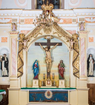 Zdjęcie nr 1: Przyścienny, architektoniczny ołtarz jednokondygnacyjny i jednoosiowy ze zwieńczeniem. Nastawa osadzona jest na cokole, w strukturze którego znajduje się prostopadłościenny ołtarz z drewnianą mensą i polichromowanym antepedium. Część środkowa retabulum, o kształcie zbliżonym do stojącego prostokąta zamkniętego trójkątnym szczytem, ujęta jest parą pilastrów osadzonych na cokołach. Zwieńczenie ołtarza przybiera formę ażurowej latarni na rzucie eliptycznym, ujętej dołem wyłamującym się gzymsem. Szczyt jest w kształcie zamkniętej, złoconej korony, wspartej na marmoryzowanych kolumienkach. Pod zwieńczenie ołtarza podwieszone jest złocone paludamentum podwiązane w górnych narożach części środkowej retabulum oraz podtrzymywane przez parę puttów i kaskadowo opadające wzdłuż pilastrów. Jego obrzeża zdobi frędzla oraz chwosty. Dodatkowo strukturę w górnej partii ołtarza zdobią: pośrodku motyw promienistej glorii z monogramem IHS z krzyżem i gorejącym sercem oraz motywy kogucich grzebieni po bokach. Pilastry zwieńczone są figurkami aniołów trzymających lichtarze, antepedium zdobi polichromowany motyw gorejącego serca Jezusa ujęty promienistą glorią oraz kłosami zbóż i gałązkami winnej latorośli, wraz z symbolami narzędzi męki Pańskiej (od lewej: kolumna biczowania i bicze, kogut, dzban z misą, młotek, obcęgi, gwoździe, lampa, rękawica, maczuga, miecz, kości do gry, trzciny, gąbka i włócznia). Pole środkowe, ujęte profilowaną, złoconą ramą, jest w kształcie leżącego prostokąta zamkniętego łukiem półkolistym. Zawiera rzeźbiarskie przedstawienie Ukrzyżowania z krucyfiksem ujętym po bokach parą figur asystencyjnych – Matki Boskiej i św. Jana Ewangelisty, ustawionych na cokołach. 
Struktura ołtarza jest utrzymana w odcieniu kremowym, partie detalu architektonicznego oraz ornamentyka są złocone i marmoryzowane w odcieniach brązu. 
 