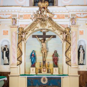 Zdjęcie nr 1: Przyścienny, architektoniczny ołtarz jednokondygnacyjny i jednoosiowy ze zwieńczeniem. Nastawa osadzona jest na cokole, w strukturze którego znajduje się prostopadłościenny ołtarz z drewnianą mensą i polichromowanym antepedium. Część środkowa retabulum, o kształcie zbliżonym do stojącego prostokąta zamkniętego trójkątnym szczytem, ujęta jest parą pilastrów osadzonych na cokołach. Zwieńczenie ołtarza przybiera formę ażurowej latarni na rzucie eliptycznym, ujętej dołem wyłamującym się gzymsem. Szczyt jest w kształcie zamkniętej, złoconej korony, wspartej na marmoryzowanych kolumienkach. Pod zwieńczenie ołtarza podwieszone jest złocone paludamentum podwiązane w górnych narożach części środkowej retabulum oraz podtrzymywane przez parę puttów i kaskadowo opadające wzdłuż pilastrów. Jego obrzeża zdobi frędzla oraz chwosty. Dodatkowo strukturę w górnej partii ołtarza zdobią: pośrodku motyw promienistej glorii z monogramem IHS z krzyżem i gorejącym sercem oraz motywy kogucich grzebieni po bokach. Pilastry zwieńczone są figurkami aniołów trzymających lichtarze, antepedium zdobi polichromowany motyw gorejącego serca Jezusa ujęty promienistą glorią oraz kłosami zbóż i gałązkami winnej latorośli, wraz z symbolami narzędzi męki Pańskiej (od lewej: kolumna biczowania i bicze, kogut, dzban z misą, młotek, obcęgi, gwoździe, lampa, rękawica, maczuga, miecz, kości do gry, trzciny, gąbka i włócznia). Pole środkowe, ujęte profilowaną, złoconą ramą, jest w kształcie leżącego prostokąta zamkniętego łukiem półkolistym. Zawiera rzeźbiarskie przedstawienie Ukrzyżowania z krucyfiksem ujętym po bokach parą figur asystencyjnych – Matki Boskiej i św. Jana Ewangelisty, ustawionych na cokołach. 
Struktura ołtarza jest utrzymana w odcieniu kremowym, partie detalu architektonicznego oraz ornamentyka są złocone i marmoryzowane w odcieniach brązu. 
 