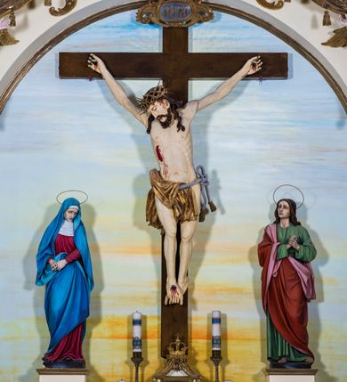 Zdjęcie nr 4: Przyścienny, architektoniczny ołtarz jednokondygnacyjny i jednoosiowy ze zwieńczeniem. Nastawa osadzona jest na cokole, w strukturze którego znajduje się prostopadłościenny ołtarz z drewnianą mensą i polichromowanym antepedium. Część środkowa retabulum, o kształcie zbliżonym do stojącego prostokąta zamkniętego trójkątnym szczytem, ujęta jest parą pilastrów osadzonych na cokołach. Zwieńczenie ołtarza przybiera formę ażurowej latarni na rzucie eliptycznym, ujętej dołem wyłamującym się gzymsem. Szczyt jest w kształcie zamkniętej, złoconej korony, wspartej na marmoryzowanych kolumienkach. Pod zwieńczenie ołtarza podwieszone jest złocone paludamentum podwiązane w górnych narożach części środkowej retabulum oraz podtrzymywane przez parę puttów i kaskadowo opadające wzdłuż pilastrów. Jego obrzeża zdobi frędzla oraz chwosty. Dodatkowo strukturę w górnej partii ołtarza zdobią: pośrodku motyw promienistej glorii z monogramem IHS z krzyżem i gorejącym sercem oraz motywy kogucich grzebieni po bokach. Pilastry zwieńczone są figurkami aniołów trzymających lichtarze, antepedium zdobi polichromowany motyw gorejącego serca Jezusa ujęty promienistą glorią oraz kłosami zbóż i gałązkami winnej latorośli, wraz z symbolami narzędzi męki Pańskiej (od lewej: kolumna biczowania i bicze, kogut, dzban z misą, młotek, obcęgi, gwoździe, lampa, rękawica, maczuga, miecz, kości do gry, trzciny, gąbka i włócznia). Pole środkowe, ujęte profilowaną, złoconą ramą, jest w kształcie leżącego prostokąta zamkniętego łukiem półkolistym. Zawiera rzeźbiarskie przedstawienie Ukrzyżowania z krucyfiksem ujętym po bokach parą figur asystencyjnych – Matki Boskiej i św. Jana Ewangelisty, ustawionych na cokołach. 
Struktura ołtarza jest utrzymana w odcieniu kremowym, partie detalu architektonicznego oraz ornamentyka są złocone i marmoryzowane w odcieniach brązu. 
 