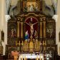 Zdjęcie nr 1: Ołtarz drewniany, architektoniczny, trójosiowy, jednokondygnacyjny ze zwieńczeniem usytuowany w połowie prezbiterium, na całej jego szerokości. Ołtarz prostopadłościenny z drewnianą mensą. Tabernakulum jest trójosiowe, osadzone na podwójnym cokole, zryzalitowane w części środkowej, podzielone kompozytowymi kolumnami, podtrzymującymi wyłamujące się nad nimi belkowanie z przerwanym przyczółkiem pośrodku. W części środkowej ruchomy tron wystawienia, wieloboczny, z rytymi literami IHS na tle glorii promienistej w jednej części i gałązkami z kwiatami w drugiej. Retabulum osadzone na wysokim cokole, z bramkami po bokach zamkniętymi łukami dwuramiennymi. Na dwiczkach malowane wizerunki św. Piotra po prawej i św. Pawła po lewej stronie. Część środkową retabulum ujmują dwie pary kompozytowych pilastrów o kanelowanych trzonech, z których środkowe cofnięte, podtrzymują przełamujące się nad nimi belkowanie i przerwany przyczółek. Zwieńczenie jest ujęte kanelowanymi pilastrami kompozytowymi z naczółkami oraz para ażurowych, ornamentacyjnych uszaków. W części środkowej jest wnęka w kształcie pionowego prostokąta zamkniętego łukiem półkolistym z rzeźbiarską grupą Ukrzyżowania z Matką Boską i św. Janem. W zwieńczeniu jest obraz „Pietas Domini" w sześciobocznej ramie. W osiach bocznych nastawy znajdują się ażurowe arkady z malowanymi wizerunkami Chrystusa u słupa i Ecce Homo. Osie zwieńczone są półkolistymi przyczółkami. W osiach bocznych przeszklone galoty z kompozycją wykonaną z tkanin oraz srebrnych i złotych nici. Dekorację ornamentalną ołtarza i tabernakulum stanowią liście akantu, girlandy i rozety. Struktura utrzymana jest w kolorze brązowym, ornamentyka i detal architektoniczy są złocone. 