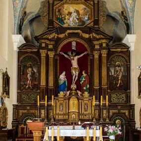 Zdjęcie nr 1: Ołtarz drewniany, architektoniczny, trójosiowy, jednokondygnacyjny ze zwieńczeniem usytuowany w połowie prezbiterium, na całej jego szerokości. Ołtarz prostopadłościenny z drewnianą mensą. Tabernakulum jest trójosiowe, osadzone na podwójnym cokole, zryzalitowane w części środkowej, podzielone kompozytowymi kolumnami, podtrzymującymi wyłamujące się nad nimi belkowanie z przerwanym przyczółkiem pośrodku. W części środkowej ruchomy tron wystawienia, wieloboczny, z rytymi literami IHS na tle glorii promienistej w jednej części i gałązkami z kwiatami w drugiej. Retabulum osadzone na wysokim cokole, z bramkami po bokach zamkniętymi łukami dwuramiennymi. Na dwiczkach malowane wizerunki św. Piotra po prawej i św. Pawła po lewej stronie. Część środkową retabulum ujmują dwie pary kompozytowych pilastrów o kanelowanych trzonech, z których środkowe cofnięte, podtrzymują przełamujące się nad nimi belkowanie i przerwany przyczółek. Zwieńczenie jest ujęte kanelowanymi pilastrami kompozytowymi z naczółkami oraz para ażurowych, ornamentacyjnych uszaków. W części środkowej jest wnęka w kształcie pionowego prostokąta zamkniętego łukiem półkolistym z rzeźbiarską grupą Ukrzyżowania z Matką Boską i św. Janem. W zwieńczeniu jest obraz „Pietas Domini" w sześciobocznej ramie. W osiach bocznych nastawy znajdują się ażurowe arkady z malowanymi wizerunkami Chrystusa u słupa i Ecce Homo. Osie zwieńczone są półkolistymi przyczółkami. W osiach bocznych przeszklone galoty z kompozycją wykonaną z tkanin oraz srebrnych i złotych nici. Dekorację ornamentalną ołtarza i tabernakulum stanowią liście akantu, girlandy i rozety. Struktura utrzymana jest w kolorze brązowym, ornamentyka i detal architektoniczy są złocone. 