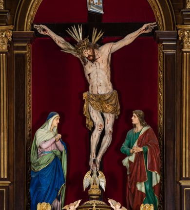 Zdjęcie nr 30: Ołtarz drewniany, architektoniczny, trójosiowy, jednokondygnacyjny ze zwieńczeniem usytuowany w połowie prezbiterium, na całej jego szerokości. Ołtarz prostopadłościenny z drewnianą mensą. Tabernakulum jest trójosiowe, osadzone na podwójnym cokole, zryzalitowane w części środkowej, podzielone kompozytowymi kolumnami, podtrzymującymi wyłamujące się nad nimi belkowanie z przerwanym przyczółkiem pośrodku. W części środkowej ruchomy tron wystawienia, wieloboczny, z rytymi literami IHS na tle glorii promienistej w jednej części i gałązkami z kwiatami w drugiej. Retabulum osadzone na wysokim cokole, z bramkami po bokach zamkniętymi łukami dwuramiennymi. Na dwiczkach malowane wizerunki św. Piotra po prawej i św. Pawła po lewej stronie. Część środkową retabulum ujmują dwie pary kompozytowych pilastrów o kanelowanych trzonech, z których środkowe cofnięte, podtrzymują przełamujące się nad nimi belkowanie i przerwany przyczółek. Zwieńczenie jest ujęte kanelowanymi pilastrami kompozytowymi z naczółkami oraz para ażurowych, ornamentacyjnych uszaków. W części środkowej jest wnęka w kształcie pionowego prostokąta zamkniętego łukiem półkolistym z rzeźbiarską grupą Ukrzyżowania z Matką Boską i św. Janem. W zwieńczeniu jest obraz „Pietas Domini&quot; w sześciobocznej ramie. W osiach bocznych nastawy znajdują się ażurowe arkady z malowanymi wizerunkami Chrystusa u słupa i Ecce Homo. Osie zwieńczone są półkolistymi przyczółkami. W osiach bocznych przeszklone galoty z kompozycją wykonaną z tkanin oraz srebrnych i złotych nici. Dekorację ornamentalną ołtarza i tabernakulum stanowią liście akantu, girlandy i rozety. Struktura utrzymana jest w kolorze brązowym, ornamentyka i detal architektoniczy są złocone. 