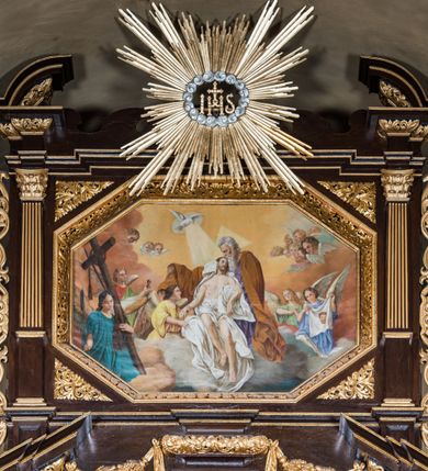Zdjęcie nr 3: Ołtarz drewniany, architektoniczny, trójosiowy, jednokondygnacyjny ze zwieńczeniem usytuowany w połowie prezbiterium, na całej jego szerokości. Ołtarz prostopadłościenny z drewnianą mensą. Tabernakulum jest trójosiowe, osadzone na podwójnym cokole, zryzalitowane w części środkowej, podzielone kompozytowymi kolumnami, podtrzymującymi wyłamujące się nad nimi belkowanie z przerwanym przyczółkiem pośrodku. W części środkowej ruchomy tron wystawienia, wieloboczny, z rytymi literami IHS na tle glorii promienistej w jednej części i gałązkami z kwiatami w drugiej. Retabulum osadzone na wysokim cokole, z bramkami po bokach zamkniętymi łukami dwuramiennymi. Na dwiczkach malowane wizerunki św. Piotra po prawej i św. Pawła po lewej stronie. Część środkową retabulum ujmują dwie pary kompozytowych pilastrów o kanelowanych trzonech, z których środkowe cofnięte, podtrzymują przełamujące się nad nimi belkowanie i przerwany przyczółek. Zwieńczenie jest ujęte kanelowanymi pilastrami kompozytowymi z naczółkami oraz para ażurowych, ornamentacyjnych uszaków. W części środkowej jest wnęka w kształcie pionowego prostokąta zamkniętego łukiem półkolistym z rzeźbiarską grupą Ukrzyżowania z Matką Boską i św. Janem. W zwieńczeniu jest obraz „Pietas Domini" w sześciobocznej ramie. W osiach bocznych nastawy znajdują się ażurowe arkady z malowanymi wizerunkami Chrystusa u słupa i Ecce Homo. Osie zwieńczone są półkolistymi przyczółkami. W osiach bocznych przeszklone galoty z kompozycją wykonaną z tkanin oraz srebrnych i złotych nici. Dekorację ornamentalną ołtarza i tabernakulum stanowią liście akantu, girlandy i rozety. Struktura utrzymana jest w kolorze brązowym, ornamentyka i detal architektoniczy są złocone. 