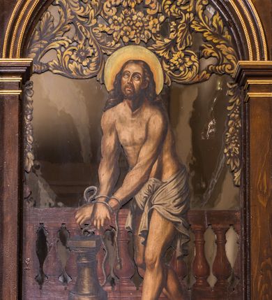 Zdjęcie nr 8: Ołtarz drewniany, architektoniczny, trójosiowy, jednokondygnacyjny ze zwieńczeniem usytuowany w połowie prezbiterium, na całej jego szerokości. Ołtarz prostopadłościenny z drewnianą mensą. Tabernakulum jest trójosiowe, osadzone na podwójnym cokole, zryzalitowane w części środkowej, podzielone kompozytowymi kolumnami, podtrzymującymi wyłamujące się nad nimi belkowanie z przerwanym przyczółkiem pośrodku. W części środkowej ruchomy tron wystawienia, wieloboczny, z rytymi literami IHS na tle glorii promienistej w jednej części i gałązkami z kwiatami w drugiej. Retabulum osadzone na wysokim cokole, z bramkami po bokach zamkniętymi łukami dwuramiennymi. Na dwiczkach malowane wizerunki św. Piotra po prawej i św. Pawła po lewej stronie. Część środkową retabulum ujmują dwie pary kompozytowych pilastrów o kanelowanych trzonech, z których środkowe cofnięte, podtrzymują przełamujące się nad nimi belkowanie i przerwany przyczółek. Zwieńczenie jest ujęte kanelowanymi pilastrami kompozytowymi z naczółkami oraz para ażurowych, ornamentacyjnych uszaków. W części środkowej jest wnęka w kształcie pionowego prostokąta zamkniętego łukiem półkolistym z rzeźbiarską grupą Ukrzyżowania z Matką Boską i św. Janem. W zwieńczeniu jest obraz „Pietas Domini&quot; w sześciobocznej ramie. W osiach bocznych nastawy znajdują się ażurowe arkady z malowanymi wizerunkami Chrystusa u słupa i Ecce Homo. Osie zwieńczone są półkolistymi przyczółkami. W osiach bocznych przeszklone galoty z kompozycją wykonaną z tkanin oraz srebrnych i złotych nici. Dekorację ornamentalną ołtarza i tabernakulum stanowią liście akantu, girlandy i rozety. Struktura utrzymana jest w kolorze brązowym, ornamentyka i detal architektoniczy są złocone. 