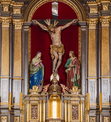 Zdjęcie nr 13: Ołtarz drewniany, architektoniczny, trójosiowy, jednokondygnacyjny ze zwieńczeniem usytuowany w połowie prezbiterium, na całej jego szerokości. Ołtarz prostopadłościenny z drewnianą mensą. Tabernakulum jest trójosiowe, osadzone na podwójnym cokole, zryzalitowane w części środkowej, podzielone kompozytowymi kolumnami, podtrzymującymi wyłamujące się nad nimi belkowanie z przerwanym przyczółkiem pośrodku. W części środkowej ruchomy tron wystawienia, wieloboczny, z rytymi literami IHS na tle glorii promienistej w jednej części i gałązkami z kwiatami w drugiej. Retabulum osadzone na wysokim cokole, z bramkami po bokach zamkniętymi łukami dwuramiennymi. Na dwiczkach malowane wizerunki św. Piotra po prawej i św. Pawła po lewej stronie. Część środkową retabulum ujmują dwie pary kompozytowych pilastrów o kanelowanych trzonech, z których środkowe cofnięte, podtrzymują przełamujące się nad nimi belkowanie i przerwany przyczółek. Zwieńczenie jest ujęte kanelowanymi pilastrami kompozytowymi z naczółkami oraz para ażurowych, ornamentacyjnych uszaków. W części środkowej jest wnęka w kształcie pionowego prostokąta zamkniętego łukiem półkolistym z rzeźbiarską grupą Ukrzyżowania z Matką Boską i św. Janem. W zwieńczeniu jest obraz „Pietas Domini&quot; w sześciobocznej ramie. W osiach bocznych nastawy znajdują się ażurowe arkady z malowanymi wizerunkami Chrystusa u słupa i Ecce Homo. Osie zwieńczone są półkolistymi przyczółkami. W osiach bocznych przeszklone galoty z kompozycją wykonaną z tkanin oraz srebrnych i złotych nici. Dekorację ornamentalną ołtarza i tabernakulum stanowią liście akantu, girlandy i rozety. Struktura utrzymana jest w kolorze brązowym, ornamentyka i detal architektoniczy są złocone. 