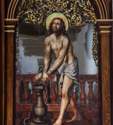 Zdjęcie nr 26: Ołtarz drewniany, architektoniczny, trójosiowy, jednokondygnacyjny ze zwieńczeniem usytuowany w połowie prezbiterium, na całej jego szerokości. Ołtarz prostopadłościenny z drewnianą mensą. Tabernakulum jest trójosiowe, osadzone na podwójnym cokole, zryzalitowane w części środkowej, podzielone kompozytowymi kolumnami, podtrzymującymi wyłamujące się nad nimi belkowanie z przerwanym przyczółkiem pośrodku. W części środkowej ruchomy tron wystawienia, wieloboczny, z rytymi literami IHS na tle glorii promienistej w jednej części i gałązkami z kwiatami w drugiej. Retabulum osadzone na wysokim cokole, z bramkami po bokach zamkniętymi łukami dwuramiennymi. Na dwiczkach malowane wizerunki św. Piotra po prawej i św. Pawła po lewej stronie. Część środkową retabulum ujmują dwie pary kompozytowych pilastrów o kanelowanych trzonech, z których środkowe cofnięte, podtrzymują przełamujące się nad nimi belkowanie i przerwany przyczółek. Zwieńczenie jest ujęte kanelowanymi pilastrami kompozytowymi z naczółkami oraz para ażurowych, ornamentacyjnych uszaków. W części środkowej jest wnęka w kształcie pionowego prostokąta zamkniętego łukiem półkolistym z rzeźbiarską grupą Ukrzyżowania z Matką Boską i św. Janem. W zwieńczeniu jest obraz „Pietas Domini&quot; w sześciobocznej ramie. W osiach bocznych nastawy znajdują się ażurowe arkady z malowanymi wizerunkami Chrystusa u słupa i Ecce Homo. Osie zwieńczone są półkolistymi przyczółkami. W osiach bocznych przeszklone galoty z kompozycją wykonaną z tkanin oraz srebrnych i złotych nici. Dekorację ornamentalną ołtarza i tabernakulum stanowią liście akantu, girlandy i rozety. Struktura utrzymana jest w kolorze brązowym, ornamentyka i detal architektoniczy są złocone. 