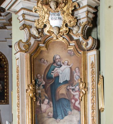 Zdjęcie nr 1: Ołtarz architektoniczny, jednokondygnacyjny, jednoosiowy, ze zwieńczeniem. Ołtarz prostopadłościenny, murowany. Retabulum o strukturze wklęsłej wzdłuż osi pionowej osadzone na niewysokim, cokole zryzalitowanym w formie pary impostów. Gzyms cokołu pośrodku ma formę półkolistego łuku nadwieszonego. Część środkowa ujęta parą wąskich filarów, licami zwróconych ukośnie w prawo, wspierających wydatny gzyms osadzony na parze spływów wolutowych. Pola cokołu retabulum zdobione ornamentyką roślinną. Na impostach para figur aniołków, stojący po lewej stronie trzyma w dłoniach zwój z napisem „KOCHAJ BOGA / I BLIZNIEGO”, stojący po prawej lewą rękę wspiera na kartuszu z napisem „POZNAJ / SIEBIE / SAMEGO”. Miedzy impostami płycina w kształcie prostokąta leżącego o wklęsłych górnych narożach i zamkniętego półkolistym łukiem nadwieszonym. W dolnej partii retabulum para uskrzydlonych główek anielskich dołem ujętych liśćmi akantu. Lica filarów zdobione motywem kampanuli. W partii belkowania, pośrodku motyw akantowego kartusza z napisem „ITE AD / IOSEPH.”, ujętego górą, dołem i po bokach motywami uskrzydlonych główek anielskich. Zwieńczenie w formie promienistej glorii z koroną zdobioną kwiatami osadzoną na obłokach. Całość flankuje para siedzących na gzymsie aniołów w dynamicznych pozach. Pole części środkowej w kształcie stojącego prostokąta ujętego górą i dołem parą zwróconych do siebie półkolistych łuków nadwieszonych z uskokami, ujęte profilowaną, złoconą ramą. Wewnątrz obraz z wizerunkiem św. Józefa. Struktura polichromowana w kolorze białym, detal architektoniczny i ornamentyka złocone i srebrzone.