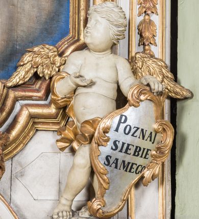 Zdjęcie nr 5: Ołtarz architektoniczny, jednokondygnacyjny, jednoosiowy, ze zwieńczeniem. Ołtarz prostopadłościenny, murowany. Retabulum o strukturze wklęsłej wzdłuż osi pionowej osadzone na niewysokim, cokole zryzalitowanym w formie pary impostów. Gzyms cokołu pośrodku ma formę półkolistego łuku nadwieszonego. Część środkowa ujęta parą wąskich filarów, licami zwróconych ukośnie w prawo, wspierających wydatny gzyms osadzony na parze spływów wolutowych. Pola cokołu retabulum zdobione ornamentyką roślinną. Na impostach para figur aniołków, stojący po lewej stronie trzyma w dłoniach zwój z napisem „KOCHAJ BOGA / I BLIZNIEGO”, stojący po prawej lewą rękę wspiera na kartuszu z napisem „POZNAJ / SIEBIE / SAMEGO”. Miedzy impostami płycina w kształcie prostokąta leżącego o wklęsłych górnych narożach i zamkniętego półkolistym łukiem nadwieszonym. W dolnej partii retabulum para uskrzydlonych główek anielskich dołem ujętych liśćmi akantu. Lica filarów zdobione motywem kampanuli. W partii belkowania, pośrodku motyw akantowego kartusza z napisem „ITE AD / IOSEPH.”, ujętego górą, dołem i po bokach motywami uskrzydlonych główek anielskich. Zwieńczenie w formie promienistej glorii z koroną zdobioną kwiatami osadzoną na obłokach. Całość flankuje para siedzących na gzymsie aniołów w dynamicznych pozach. Pole części środkowej w kształcie stojącego prostokąta ujętego górą i dołem parą zwróconych do siebie półkolistych łuków nadwieszonych z uskokami, ujęte profilowaną, złoconą ramą. Wewnątrz obraz z wizerunkiem św. Józefa. Struktura polichromowana w kolorze białym, detal architektoniczny i ornamentyka złocone i srebrzone.