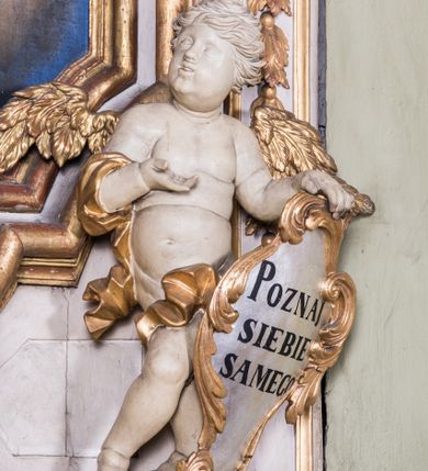 Zdjęcie nr 3: Ołtarz architektoniczny, jednokondygnacyjny, jednoosiowy, ze zwieńczeniem. Ołtarz prostopadłościenny, murowany. Retabulum o strukturze wklęsłej wzdłuż osi pionowej osadzone na niewysokim, cokole zryzalitowanym w formie pary impostów. Gzyms cokołu pośrodku ma formę półkolistego łuku nadwieszonego. Część środkowa ujęta parą wąskich filarów, licami zwróconych ukośnie w prawo, wspierających wydatny gzyms osadzony na parze spływów wolutowych. Pola cokołu retabulum zdobione ornamentyką roślinną. Na impostach para figur aniołków, stojący po lewej stronie trzyma w dłoniach zwój z napisem „KOCHAJ BOGA / I BLIZNIEGO”, stojący po prawej lewą rękę wspiera na kartuszu z napisem „POZNAJ / SIEBIE / SAMEGO”. Miedzy impostami płycina w kształcie prostokąta leżącego o wklęsłych górnych narożach i zamkniętego półkolistym łukiem nadwieszonym. W dolnej partii retabulum para uskrzydlonych główek anielskich dołem ujętych liśćmi akantu. Lica filarów zdobione motywem kampanuli. W partii belkowania, pośrodku motyw akantowego kartusza z napisem „ITE AD / IOSEPH.”, ujętego górą, dołem i po bokach motywami uskrzydlonych główek anielskich. Zwieńczenie w formie promienistej glorii z koroną zdobioną kwiatami osadzoną na obłokach. Całość flankuje para siedzących na gzymsie aniołów w dynamicznych pozach. Pole części środkowej w kształcie stojącego prostokąta ujętego górą i dołem parą zwróconych do siebie półkolistych łuków nadwieszonych z uskokami, ujęte profilowaną, złoconą ramą. Wewnątrz obraz z wizerunkiem św. Józefa. Struktura polichromowana w kolorze białym, detal architektoniczny i ornamentyka złocone i srebrzone.