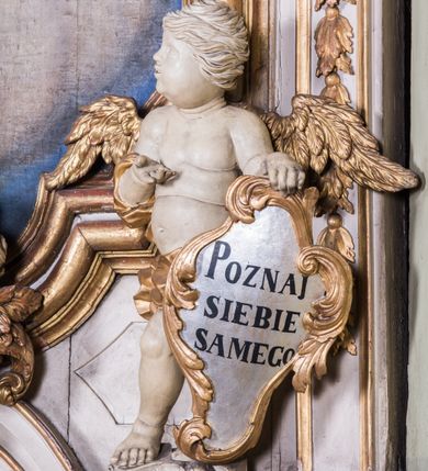 Zdjęcie nr 4: Ołtarz architektoniczny, jednokondygnacyjny, jednoosiowy, ze zwieńczeniem. Ołtarz prostopadłościenny, murowany. Retabulum o strukturze wklęsłej wzdłuż osi pionowej osadzone na niewysokim, cokole zryzalitowanym w formie pary impostów. Gzyms cokołu pośrodku ma formę półkolistego łuku nadwieszonego. Część środkowa ujęta parą wąskich filarów, licami zwróconych ukośnie w prawo, wspierających wydatny gzyms osadzony na parze spływów wolutowych. Pola cokołu retabulum zdobione ornamentyką roślinną. Na impostach para figur aniołków, stojący po lewej stronie trzyma w dłoniach zwój z napisem „KOCHAJ BOGA / I BLIZNIEGO”, stojący po prawej lewą rękę wspiera na kartuszu z napisem „POZNAJ / SIEBIE / SAMEGO”. Miedzy impostami płycina w kształcie prostokąta leżącego o wklęsłych górnych narożach i zamkniętego półkolistym łukiem nadwieszonym. W dolnej partii retabulum para uskrzydlonych główek anielskich dołem ujętych liśćmi akantu. Lica filarów zdobione motywem kampanuli. W partii belkowania, pośrodku motyw akantowego kartusza z napisem „ITE AD / IOSEPH.”, ujętego górą, dołem i po bokach motywami uskrzydlonych główek anielskich. Zwieńczenie w formie promienistej glorii z koroną zdobioną kwiatami osadzoną na obłokach. Całość flankuje para siedzących na gzymsie aniołów w dynamicznych pozach. Pole części środkowej w kształcie stojącego prostokąta ujętego górą i dołem parą zwróconych do siebie półkolistych łuków nadwieszonych z uskokami, ujęte profilowaną, złoconą ramą. Wewnątrz obraz z wizerunkiem św. Józefa. Struktura polichromowana w kolorze białym, detal architektoniczny i ornamentyka złocone i srebrzone.