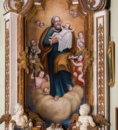 Zdjęcie nr 13: Ołtarz architektoniczny, jednokondygnacyjny, jednoosiowy, ze zwieńczeniem. Ołtarz prostopadłościenny, murowany. Retabulum o strukturze wklęsłej wzdłuż osi pionowej osadzone na niewysokim, cokole zryzalitowanym w formie pary impostów. Gzyms cokołu pośrodku ma formę półkolistego łuku nadwieszonego. Część środkowa ujęta parą wąskich filarów, licami zwróconych ukośnie w prawo, wspierających wydatny gzyms osadzony na parze spływów wolutowych. Pola cokołu retabulum zdobione ornamentyką roślinną. Na impostach para figur aniołków, stojący po lewej stronie trzyma w dłoniach zwój z napisem „KOCHAJ BOGA / I BLIZNIEGO”, stojący po prawej lewą rękę wspiera na kartuszu z napisem „POZNAJ / SIEBIE / SAMEGO”. Miedzy impostami płycina w kształcie prostokąta leżącego o wklęsłych górnych narożach i zamkniętego półkolistym łukiem nadwieszonym. W dolnej partii retabulum para uskrzydlonych główek anielskich dołem ujętych liśćmi akantu. Lica filarów zdobione motywem kampanuli. W partii belkowania, pośrodku motyw akantowego kartusza z napisem „ITE AD / IOSEPH.”, ujętego górą, dołem i po bokach motywami uskrzydlonych główek anielskich. Zwieńczenie w formie promienistej glorii z koroną zdobioną kwiatami osadzoną na obłokach. Całość flankuje para siedzących na gzymsie aniołów w dynamicznych pozach. Pole części środkowej w kształcie stojącego prostokąta ujętego górą i dołem parą zwróconych do siebie półkolistych łuków nadwieszonych z uskokami, ujęte profilowaną, złoconą ramą. Wewnątrz obraz z wizerunkiem św. Józefa. Struktura polichromowana w kolorze białym, detal architektoniczny i ornamentyka złocone i srebrzone.