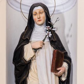 Zdjęcie nr 1: Całopostaciowa, pełnoplastyczna figura zwróconej na wprost św. Katarzyny Sieneńskiej stojącej w kontrapoście na niewysokiej, prostopadłościennej podstawie o ściętych narożach. Lekko przechyloną w prawo głowę charakteryzuje pociągła twarz o delikatnych rysach z długim, prostym nosem, nieznacznie opuszczonymi powiekami, kształtnym wykrojem ust i zaróżowionymi policzkami. Święta ubrana jest w habit dominikański ze szkaplerzem na habicie oraz czarnym płaszczem, na stopach ma czarne buty, pod welonem natomiast białą podwikę. W prawej, wspartej na piersiach ręce trzyma kwiat białej lilii, w lewej, opuszczonej wzdłuż ciała zamkniętą księgę. Głowę świętej okala wąska aureola.    

