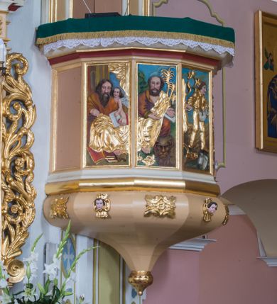 Zdjęcie nr 1: Wisząca, przyścienna ambona składa się z kosza, zaplecka i baldachimu. Dojście do kosza prowadzi przez dwuskrzydłowe drzwi usytuowane w zaplecku. Kształt kosza oparto na planie siedmiu boków z dziesięcioboku, ustawionych na wałku, z podwieszeniem w formie zbliżonej do stożka, zakończonego szyszką oraz dekorowanym rozetami i uskrzydlonymi główkami anielskimi. Ścianki kosza artykułowano prostokątnymi, obramienionymi płycinami z pięcioma płaskorzeźbionymi przedstawieniam czterech ewangelistów i siewcy. Każdego ewangelistę identyfikuje jego atrybut. Siewca, umieszczony na trzeciej płycinie, został ukazany jako młody mężczyzna, który idąc przez zaorane pole rzuca w nie ziarno. U jego stóp widać pług oraz worek ze zbożem na zasiew. Parapet kosza uzyskał formę gzymsu. Zaplecek został ujęty profilowaną ramą. W jego pole wpisano prostokątne, dwuskrzydłowe drzwi w profilowanym obramieniu. Baldachim uzyskał rzut analogiczny do kosza ambony. Płaskie podniebie z wyobrażeniem gołębicy Ducha Świętego na tle złocistych promieni ujmuje profilowany, łamany gzyms, ponad którym poprowadzono kopulasty dach. Na jego szczycie ustawiono rzeźbę Mojżesza trzymającego tablice Dekalogu. Struktura ambony została polichromowana w kolorze beżowym, z białymi i czerwonymi profilami, oraz pozłacanymi detalami, profilami i ornamentyką. Płaskorzeźby na koszu oraz figura Mojżesza otrzymały naturalistyczną polichromię.