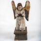 Zdjęcie nr 1: Pełnoplastyczna figura ukazuje przyklękającego na prawe kolano uskrzydlonego anioła. Anioł o lekko pochylonej głowie do przodu ma modlitewnie złożone ręce przed sobą. Jego owalną twarz o jasnej karnacji, drobnym nosie i ustach otaczają krótkie brązowe włosy. Postać ubrana jest w białą, luźną tunikę. Umieszono ją na prostopadłościennym drewnianym postumencie zaopatrzonym w niski profilowany cokół oraz gzyms. 