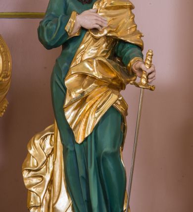 Zdjęcie nr 2: Rzeźba św. Pawła została ścięta z tyłu i wydrążona oraz ustawiona na kwadratowej podstawie. Apostoł został ukazany w trzech czwartych w lewo, w kontrapoście. W wyciągniętej w bok lewej ręce trzyma miecz zwrócony ostrzem w dół, prawą zaś wspiera na piersi. Twarz Pawła jest szczupła, o głęboko osadzonych oczach, prostym nosie i rozchylonych ustach. Okala ją długa skręcona broda opadająca na pierś oraz krótkie, kręcone włosy. Apostoł jest ubrany w zieloną tunikę, przylegająca do ciała o pozłacanych mankietach oraz płaszcz zawieszony na lewym ramieniu, opadający z przodu postaci i na prawy bok. Polichromia ciała jest naturalistyczna.