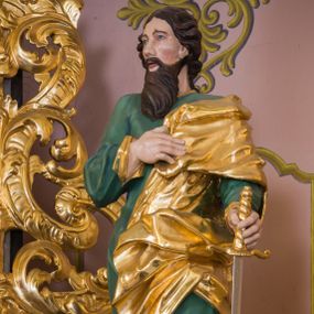 Zdjęcie nr 1: Rzeźba św. Pawła została ścięta z tyłu i wydrążona oraz ustawiona na kwadratowej podstawie. Apostoł został ukazany w trzech czwartych w lewo, w kontrapoście. W wyciągniętej w bok lewej ręce trzyma miecz zwrócony ostrzem w dół, prawą zaś wspiera na piersi. Twarz Pawła jest szczupła, o głęboko osadzonych oczach, prostym nosie i rozchylonych ustach. Okala ją długa skręcona broda opadająca na pierś oraz krótkie, kręcone włosy. Apostoł jest ubrany w zieloną tunikę, przylegająca do ciała o pozłacanych mankietach oraz płaszcz zawieszony na lewym ramieniu, opadający z przodu postaci i na prawy bok. Polichromia ciała jest naturalistyczna.