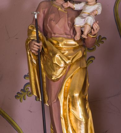 Zdjęcie nr 8: Jednokondygnacyjna nastawa ze zwieńczeniem uzyskała architektoniczną strukturę wzbogaconą o  flankujące ją bramkami. Współczesny marmurowy stipes ołtarzowy wspierający mensę uzyskał formę prostopadłościanu z licem artykułowanym dwiema półkolumienkami. Na mensie ustawiono tabernakulum w formie drewnianej skrzynki, obitej trybowaną blachą. Drzwiczki uzyskały kształt stojącego prostokąta zamkniętego łukiem półkolistym. W ich polu wyobrażono kielich z hostią w glorii, ujęty trybowanym winnym gronem i aplikowanymi kłosami zbóż. Z dwóch stron drzwiczek widnieje trybowana dekoracja w postaci winnego grona. Na tabernakulum usytuowano tron wystawienia, w postaci obrotowej niszy ujętej dwiema parami kolumienek podtrzymujących gzyms wyłamany pośrodku na kształt łuku odcinkowego oraz cokół z figurką baranka na księdze z siedmioma pieczęciami, podtrzymywany przez dwa spływy wolutowe. Tabernakulum ujęte zostało dwoma postumentami dekorowanymi z przodu rozetami. Ustawiono na nich figury klęczących aniołów. Nastawa ujęta została dwiema parami kolumn o kapitelach kompozytowych ustawionych na cokołach dekorowanych płycinami z ornamentem roślinnym, podtrzymujących pełne belkowanie z silnie wysuniętym gzymsem, oraz zewnętrzną parą cofniętych w tył kolumn. W polu głównym usytuowano obraz z przedstawieniem Zmartwychwstałego Chrystusa ze św. Janem Chrzcicielem i św. Janem Ewangelistą, ujęty profilowaną ramą w formie stojącego prostokąta zamkniętego łukiem odcinkowych nadwieszonym. Kondygnacja ujęta została po bokach uszami utworzonymi z karbowanej wstęgi i akantu. Zwieńczenie nastawy ustawiono na schodkowym, zwężającym się cokole, dekorowanym medalionem z monogramem Marii oraz anthemionami. Ujmują je dwie pary kolumienek o kapitelach kompozytowych podtrzymujących gzyms wyłamujący się po środku na kształt łuku półkolistego, dekorowany wicią roślinną. W polu zwieńczenia znalazł się obraz w formie stojącego owalu z przedstawieniem Dzieciątka Jezus prezentującego krzyż, ujęty profilowaną ramą dekorowaną ornamentem roślinnym. Zwieńczenie flankują stojące na gzymsie figury św. Józefa z Dzieciątkiem i Symeona z Dzieciątkiem. Nastawę flankują znajdujące się przy ścianie para kolumn i para półkolumn ustawionych na dwustrefowych cokołach, dźwigających pełne belkowanie, na którym siedzą dwa putta. Pomiędzy cokołem nastawy i zewnętrznych podpór ulokowano wygięte listwy tworzące bramki, na których stoją figury św. Piotra i św. Pawła. Struktura retabulum jest polichromowana w kolorze beżowym, z białymi i czerwonymi profilami i płycinami. Kolumny, ornamentyka i profile zostały pozłocone.