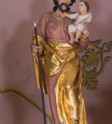 Zdjęcie nr 7: Jednokondygnacyjna nastawa ze zwieńczeniem uzyskała architektoniczną strukturę wzbogaconą o  flankujące ją bramkami. Współczesny marmurowy stipes ołtarzowy wspierający mensę uzyskał formę prostopadłościanu z licem artykułowanym dwiema półkolumienkami. Na mensie ustawiono tabernakulum w formie drewnianej skrzynki, obitej trybowaną blachą. Drzwiczki uzyskały kształt stojącego prostokąta zamkniętego łukiem półkolistym. W ich polu wyobrażono kielich z hostią w glorii, ujęty trybowanym winnym gronem i aplikowanymi kłosami zbóż. Z dwóch stron drzwiczek widnieje trybowana dekoracja w postaci winnego grona. Na tabernakulum usytuowano tron wystawienia, w postaci obrotowej niszy ujętej dwiema parami kolumienek podtrzymujących gzyms wyłamany pośrodku na kształt łuku odcinkowego oraz cokół z figurką baranka na księdze z siedmioma pieczęciami, podtrzymywany przez dwa spływy wolutowe. Tabernakulum ujęte zostało dwoma postumentami dekorowanymi z przodu rozetami. Ustawiono na nich figury klęczących aniołów. Nastawa ujęta została dwiema parami kolumn o kapitelach kompozytowych ustawionych na cokołach dekorowanych płycinami z ornamentem roślinnym, podtrzymujących pełne belkowanie z silnie wysuniętym gzymsem, oraz zewnętrzną parą cofniętych w tył kolumn. W polu głównym usytuowano obraz z przedstawieniem Zmartwychwstałego Chrystusa ze św. Janem Chrzcicielem i św. Janem Ewangelistą, ujęty profilowaną ramą w formie stojącego prostokąta zamkniętego łukiem odcinkowych nadwieszonym. Kondygnacja ujęta została po bokach uszami utworzonymi z karbowanej wstęgi i akantu. Zwieńczenie nastawy ustawiono na schodkowym, zwężającym się cokole, dekorowanym medalionem z monogramem Marii oraz anthemionami. Ujmują je dwie pary kolumienek o kapitelach kompozytowych podtrzymujących gzyms wyłamujący się po środku na kształt łuku półkolistego, dekorowany wicią roślinną. W polu zwieńczenia znalazł się obraz w formie stojącego owalu z przedstawieniem Dzieciątka Jezus prezentującego krzyż, ujęty profilowaną ramą dekorowaną ornamentem roślinnym. Zwieńczenie flankują stojące na gzymsie figury św. Józefa z Dzieciątkiem i Symeona z Dzieciątkiem. Nastawę flankują znajdujące się przy ścianie para kolumn i para półkolumn ustawionych na dwustrefowych cokołach, dźwigających pełne belkowanie, na którym siedzą dwa putta. Pomiędzy cokołem nastawy i zewnętrznych podpór ulokowano wygięte listwy tworzące bramki, na których stoją figury św. Piotra i św. Pawła. Struktura retabulum jest polichromowana w kolorze beżowym, z białymi i czerwonymi profilami i płycinami. Kolumny, ornamentyka i profile zostały pozłocone.