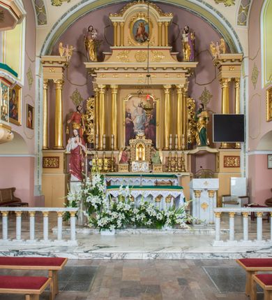 Zdjęcie nr 2: Jednokondygnacyjna nastawa ze zwieńczeniem uzyskała architektoniczną strukturę wzbogaconą o  flankujące ją bramkami. Współczesny marmurowy stipes ołtarzowy wspierający mensę uzyskał formę prostopadłościanu z licem artykułowanym dwiema półkolumienkami. Na mensie ustawiono tabernakulum w formie drewnianej skrzynki, obitej trybowaną blachą. Drzwiczki uzyskały kształt stojącego prostokąta zamkniętego łukiem półkolistym. W ich polu wyobrażono kielich z hostią w glorii, ujęty trybowanym winnym gronem i aplikowanymi kłosami zbóż. Z dwóch stron drzwiczek widnieje trybowana dekoracja w postaci winnego grona. Na tabernakulum usytuowano tron wystawienia, w postaci obrotowej niszy ujętej dwiema parami kolumienek podtrzymujących gzyms wyłamany pośrodku na kształt łuku odcinkowego oraz cokół z figurką baranka na księdze z siedmioma pieczęciami, podtrzymywany przez dwa spływy wolutowe. Tabernakulum ujęte zostało dwoma postumentami dekorowanymi z przodu rozetami. Ustawiono na nich figury klęczących aniołów. Nastawa ujęta została dwiema parami kolumn o kapitelach kompozytowych ustawionych na cokołach dekorowanych płycinami z ornamentem roślinnym, podtrzymujących pełne belkowanie z silnie wysuniętym gzymsem, oraz zewnętrzną parą cofniętych w tył kolumn. W polu głównym usytuowano obraz z przedstawieniem Zmartwychwstałego Chrystusa ze św. Janem Chrzcicielem i św. Janem Ewangelistą, ujęty profilowaną ramą w formie stojącego prostokąta zamkniętego łukiem odcinkowych nadwieszonym. Kondygnacja ujęta została po bokach uszami utworzonymi z karbowanej wstęgi i akantu. Zwieńczenie nastawy ustawiono na schodkowym, zwężającym się cokole, dekorowanym medalionem z monogramem Marii oraz anthemionami. Ujmują je dwie pary kolumienek o kapitelach kompozytowych podtrzymujących gzyms wyłamujący się po środku na kształt łuku półkolistego, dekorowany wicią roślinną. W polu zwieńczenia znalazł się obraz w formie stojącego owalu z przedstawieniem Dzieciątka Jezus prezentującego krzyż, ujęty profilowaną ramą dekorowaną ornamentem roślinnym. Zwieńczenie flankują stojące na gzymsie figury św. Józefa z Dzieciątkiem i Symeona z Dzieciątkiem. Nastawę flankują znajdujące się przy ścianie para kolumn i para półkolumn ustawionych na dwustrefowych cokołach, dźwigających pełne belkowanie, na którym siedzą dwa putta. Pomiędzy cokołem nastawy i zewnętrznych podpór ulokowano wygięte listwy tworzące bramki, na których stoją figury św. Piotra i św. Pawła. Struktura retabulum jest polichromowana w kolorze beżowym, z białymi i czerwonymi profilami i płycinami. Kolumny, ornamentyka i profile zostały pozłocone.