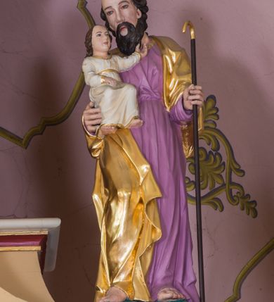 Zdjęcie nr 12: Jednokondygnacyjna nastawa ze zwieńczeniem uzyskała architektoniczną strukturę wzbogaconą o  flankujące ją bramkami. Współczesny marmurowy stipes ołtarzowy wspierający mensę uzyskał formę prostopadłościanu z licem artykułowanym dwiema półkolumienkami. Na mensie ustawiono tabernakulum w formie drewnianej skrzynki, obitej trybowaną blachą. Drzwiczki uzyskały kształt stojącego prostokąta zamkniętego łukiem półkolistym. W ich polu wyobrażono kielich z hostią w glorii, ujęty trybowanym winnym gronem i aplikowanymi kłosami zbóż. Z dwóch stron drzwiczek widnieje trybowana dekoracja w postaci winnego grona. Na tabernakulum usytuowano tron wystawienia, w postaci obrotowej niszy ujętej dwiema parami kolumienek podtrzymujących gzyms wyłamany pośrodku na kształt łuku odcinkowego oraz cokół z figurką baranka na księdze z siedmioma pieczęciami, podtrzymywany przez dwa spływy wolutowe. Tabernakulum ujęte zostało dwoma postumentami dekorowanymi z przodu rozetami. Ustawiono na nich figury klęczących aniołów. Nastawa ujęta została dwiema parami kolumn o kapitelach kompozytowych ustawionych na cokołach dekorowanych płycinami z ornamentem roślinnym, podtrzymujących pełne belkowanie z silnie wysuniętym gzymsem, oraz zewnętrzną parą cofniętych w tył kolumn. W polu głównym usytuowano obraz z przedstawieniem Zmartwychwstałego Chrystusa ze św. Janem Chrzcicielem i św. Janem Ewangelistą, ujęty profilowaną ramą w formie stojącego prostokąta zamkniętego łukiem odcinkowych nadwieszonym. Kondygnacja ujęta została po bokach uszami utworzonymi z karbowanej wstęgi i akantu. Zwieńczenie nastawy ustawiono na schodkowym, zwężającym się cokole, dekorowanym medalionem z monogramem Marii oraz anthemionami. Ujmują je dwie pary kolumienek o kapitelach kompozytowych podtrzymujących gzyms wyłamujący się po środku na kształt łuku półkolistego, dekorowany wicią roślinną. W polu zwieńczenia znalazł się obraz w formie stojącego owalu z przedstawieniem Dzieciątka Jezus prezentującego krzyż, ujęty profilowaną ramą dekorowaną ornamentem roślinnym. Zwieńczenie flankują stojące na gzymsie figury św. Józefa z Dzieciątkiem i Symeona z Dzieciątkiem. Nastawę flankują znajdujące się przy ścianie para kolumn i para półkolumn ustawionych na dwustrefowych cokołach, dźwigających pełne belkowanie, na którym siedzą dwa putta. Pomiędzy cokołem nastawy i zewnętrznych podpór ulokowano wygięte listwy tworzące bramki, na których stoją figury św. Piotra i św. Pawła. Struktura retabulum jest polichromowana w kolorze beżowym, z białymi i czerwonymi profilami i płycinami. Kolumny, ornamentyka i profile zostały pozłocone.