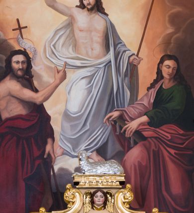 Zdjęcie nr 21: Jednokondygnacyjna nastawa ze zwieńczeniem uzyskała architektoniczną strukturę wzbogaconą o  flankujące ją bramkami. Współczesny marmurowy stipes ołtarzowy wspierający mensę uzyskał formę prostopadłościanu z licem artykułowanym dwiema półkolumienkami. Na mensie ustawiono tabernakulum w formie drewnianej skrzynki, obitej trybowaną blachą. Drzwiczki uzyskały kształt stojącego prostokąta zamkniętego łukiem półkolistym. W ich polu wyobrażono kielich z hostią w glorii, ujęty trybowanym winnym gronem i aplikowanymi kłosami zbóż. Z dwóch stron drzwiczek widnieje trybowana dekoracja w postaci winnego grona. Na tabernakulum usytuowano tron wystawienia, w postaci obrotowej niszy ujętej dwiema parami kolumienek podtrzymujących gzyms wyłamany pośrodku na kształt łuku odcinkowego oraz cokół z figurką baranka na księdze z siedmioma pieczęciami, podtrzymywany przez dwa spływy wolutowe. Tabernakulum ujęte zostało dwoma postumentami dekorowanymi z przodu rozetami. Ustawiono na nich figury klęczących aniołów. Nastawa ujęta została dwiema parami kolumn o kapitelach kompozytowych ustawionych na cokołach dekorowanych płycinami z ornamentem roślinnym, podtrzymujących pełne belkowanie z silnie wysuniętym gzymsem, oraz zewnętrzną parą cofniętych w tył kolumn. W polu głównym usytuowano obraz z przedstawieniem Zmartwychwstałego Chrystusa ze św. Janem Chrzcicielem i św. Janem Ewangelistą, ujęty profilowaną ramą w formie stojącego prostokąta zamkniętego łukiem odcinkowych nadwieszonym. Kondygnacja ujęta została po bokach uszami utworzonymi z karbowanej wstęgi i akantu. Zwieńczenie nastawy ustawiono na schodkowym, zwężającym się cokole, dekorowanym medalionem z monogramem Marii oraz anthemionami. Ujmują je dwie pary kolumienek o kapitelach kompozytowych podtrzymujących gzyms wyłamujący się po środku na kształt łuku półkolistego, dekorowany wicią roślinną. W polu zwieńczenia znalazł się obraz w formie stojącego owalu z przedstawieniem Dzieciątka Jezus prezentującego krzyż, ujęty profilowaną ramą dekorowaną ornamentem roślinnym. Zwieńczenie flankują stojące na gzymsie figury św. Józefa z Dzieciątkiem i Symeona z Dzieciątkiem. Nastawę flankują znajdujące się przy ścianie para kolumn i para półkolumn ustawionych na dwustrefowych cokołach, dźwigających pełne belkowanie, na którym siedzą dwa putta. Pomiędzy cokołem nastawy i zewnętrznych podpór ulokowano wygięte listwy tworzące bramki, na których stoją figury św. Piotra i św. Pawła. Struktura retabulum jest polichromowana w kolorze beżowym, z białymi i czerwonymi profilami i płycinami. Kolumny, ornamentyka i profile zostały pozłocone.