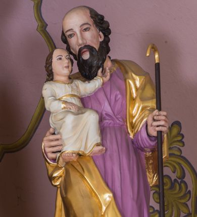 Zdjęcie nr 1: Rzeźba św. Joachima została ścięta z tyłu i wydrążona. Joachim został ujęty frontalnie, w kontrapoście, z głową przechyloną w lewo. Na prawym przedramieniu podtrzymuje Dzieciątko, a w lewej ręce trzyma zakrzywioną laskę. Ma pociągłą twarz o wysokim czole, migdałowatych oczach, prostym nosie, okoloną brodą i włosami po bokach głowy. Na czubku głowy widoczna jest łysina. Święty ubrany jest w fioletową tunikę oraz pozłocony płaszcz zarzucony na ramiona, opadający na plecy i na prawy bok. Spod tuniki widać jego bose stopy. Dzieciątko ukazano w pozycji siedzącej, lewą rączką wyciąga w stronę twarzy Symeona, a prawą przed siebie. Mały Jezus ubrany jest w białą tunikę ze złotą lamówką.