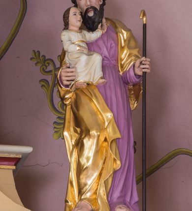 Zdjęcie nr 2: Rzeźba św. Joachima została ścięta z tyłu i wydrążona. Joachim został ujęty frontalnie, w kontrapoście, z głową przechyloną w lewo. Na prawym przedramieniu podtrzymuje Dzieciątko, a w lewej ręce trzyma zakrzywioną laskę. Ma pociągłą twarz o wysokim czole, migdałowatych oczach, prostym nosie, okoloną brodą i włosami po bokach głowy. Na czubku głowy widoczna jest łysina. Święty ubrany jest w fioletową tunikę oraz pozłocony płaszcz zarzucony na ramiona, opadający na plecy i na prawy bok. Spod tuniki widać jego bose stopy. Dzieciątko ukazano w pozycji siedzącej, lewą rączką wyciąga w stronę twarzy Symeona, a prawą przed siebie. Mały Jezus ubrany jest w białą tunikę ze złotą lamówką.