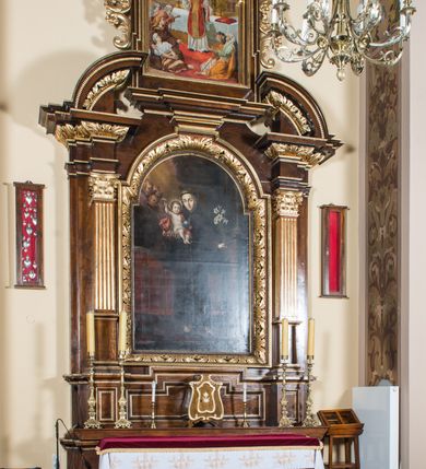 Zdjęcie nr 4: Ołtarz architektoniczny, jednokondygnacyjny, jednoosiowy, ze zwieńczeniem. Ołtarz prostopadłościenny z drewnianą mensą i drewnianym antepedium artykułowanym trzema prostokątnymi płycinami. Retabulum osadzone na nieznacznie zryzalitowanym cokole, lekko wstępującym pośrodku w kolejną partię retabulum. Część środkową ołtarza ujmuje para filarów o czworobocznym przekroju, ustawionych na tle zdwojonych pilastrów, osadzonych na wysokich cokołach i podtrzymujących przerwane belkowanie ze wspartym na nim przerwanym, półkolistym przyczółkiem. Część środkowa belkowania jest wyniesiona nieco wyżej. Pole części środkowej ma kształt stojącego prostokąta zamkniętego półkolistym łukiem nadwieszonym. Osadzone na wyłamującym się pośrodku gzymsie zwieńczenie jest w postaci stojącego prostokąta wypełnionego płyciną z uszakami w narożach, zamkniętą odcinkowym łukiem nadwieszonym. Pole środkowe ma formę zbliżoną do kwadratu zamkniętego półkolistym łukiem nadwieszonym. W szczytach łuków znajduje się zwornik na którym osadzony jest niewielki, prostopadłościenny cokolik. Zwieńczenie domyka szczyt w formie przerwanego, trójkątnego, wklęsłego przyczółka osadzonego na przerwanym belkowaniu. Środkową płycinę antepedium zdobi płaskorzeźbiony i złocony motyw Oka Opatrzności Bożej wpisany w owal i ujęty parą gałązek laurowych. Boki zwieńczenia zdobi para ażurowych, ornamentalnych uszaków. W szczycie, po bokach, na przerwanym przyczółku jest para płonących wazonów, pośrodku natomiast, na cokoliku znajduje się motyw otwartej księgi z napisem: „Si / quaeris / miracula” oraz kwiaty lilii i krzyż. W polu części środkowej przedstawiono wizerunek św. Antoniego Padewskiego. W zwieńczeniu natomiast wyobrażenie św. Dydaka. Struktura retabulum utrzymana jest w kolorystyce pokostowanego drewna, partie detalu architektonicznego i ornamentyka są złocone i srebrzone.   