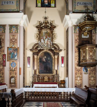 Zdjęcie nr 2: Ołtarz architektoniczny, jednokondygnacyjny, jednoosiowy, ze zwieńczeniem. Ołtarz prostopadłościenny z drewnianą mensą i drewnianym antepedium artykułowanym trzema prostokątnymi płycinami. Retabulum osadzone na nieznacznie zryzalitowanym cokole, lekko wstępującym pośrodku w kolejną partię retabulum. Część środkową ołtarza ujmuje para filarów o czworobocznym przekroju, ustawionych na tle zdwojonych pilastrów, osadzonych na wysokich cokołach i podtrzymujących przerwane belkowanie ze wspartym na nim przerwanym, półkolistym przyczółkiem. Część środkowa belkowania jest wyniesiona nieco wyżej. Pole części środkowej ma kształt stojącego prostokąta zamkniętego półkolistym łukiem nadwieszonym. Osadzone na wyłamującym się pośrodku gzymsie zwieńczenie jest w postaci stojącego prostokąta wypełnionego płyciną z uszakami w narożach, zamkniętą odcinkowym łukiem nadwieszonym. Pole środkowe ma formę zbliżoną do kwadratu zamkniętego półkolistym łukiem nadwieszonym. W szczytach łuków znajduje się zwornik na którym osadzony jest niewielki, prostopadłościenny cokolik. Zwieńczenie domyka szczyt w formie przerwanego, trójkątnego, wklęsłego przyczółka osadzonego na przerwanym belkowaniu. Środkową płycinę antepedium zdobi płaskorzeźbiony i złocony motyw Oka Opatrzności Bożej wpisany w owal i ujęty parą gałązek laurowych. Boki zwieńczenia zdobi para ażurowych, ornamentalnych uszaków. W szczycie, po bokach, na przerwanym przyczółku jest para płonących wazonów, pośrodku natomiast, na cokoliku znajduje się motyw otwartej księgi z napisem: „Si / quaeris / miracula” oraz kwiaty lilii i krzyż. W polu części środkowej przedstawiono wizerunek św. Antoniego Padewskiego. W zwieńczeniu natomiast wyobrażenie św. Dydaka. Struktura retabulum utrzymana jest w kolorystyce pokostowanego drewna, partie detalu architektonicznego i ornamentyka są złocone i srebrzone.   