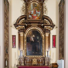 Zdjęcie nr 1: Ołtarz architektoniczny, jednokondygnacyjny, jednoosiowy, ze zwieńczeniem. Ołtarz prostopadłościenny z drewnianą mensą i drewnianym antepedium artykułowanym trzema prostokątnymi płycinami. Retabulum osadzone na nieznacznie zryzalitowanym cokole, lekko wstępującym pośrodku w kolejną partię retabulum. Część środkową ołtarza ujmuje para filarów o czworobocznym przekroju, ustawionych na tle zdwojonych pilastrów, osadzonych na wysokich cokołach i podtrzymujących przerwane belkowanie ze wspartym na nim przerwanym, półkolistym przyczółkiem. Część środkowa belkowania jest wyniesiona nieco wyżej. Pole części środkowej ma kształt stojącego prostokąta zamkniętego półkolistym łukiem nadwieszonym. Osadzone na wyłamującym się pośrodku gzymsie zwieńczenie jest w postaci stojącego prostokąta wypełnionego płyciną z uszakami w narożach, zamkniętą odcinkowym łukiem nadwieszonym. Pole środkowe ma formę zbliżoną do kwadratu zamkniętego półkolistym łukiem nadwieszonym. W szczytach łuków znajduje się zwornik na którym osadzony jest niewielki, prostopadłościenny cokolik. Zwieńczenie domyka szczyt w formie przerwanego, trójkątnego, wklęsłego przyczółka osadzonego na przerwanym belkowaniu. Środkową płycinę antepedium zdobi płaskorzeźbiony i złocony motyw Oka Opatrzności Bożej wpisany w owal i ujęty parą gałązek laurowych. Boki zwieńczenia zdobi para ażurowych, ornamentalnych uszaków. W szczycie, po bokach, na przerwanym przyczółku jest para płonących wazonów, pośrodku natomiast, na cokoliku znajduje się motyw otwartej księgi z napisem: „Si / quaeris / miracula” oraz kwiaty lilii i krzyż. W polu części środkowej przedstawiono wizerunek św. Antoniego Padewskiego. W zwieńczeniu natomiast wyobrażenie św. Dydaka. Struktura retabulum utrzymana jest w kolorystyce pokostowanego drewna, partie detalu architektonicznego i ornamentyka są złocone i srebrzone.   