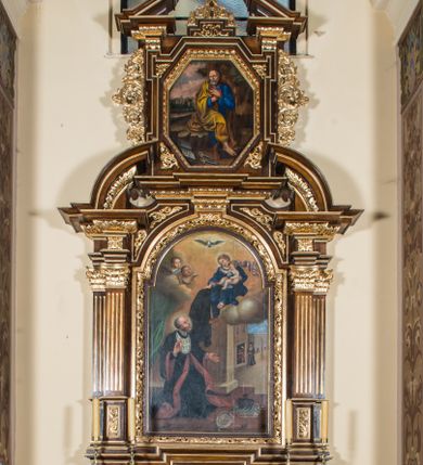 Zdjęcie nr 1: Ołtarz architektoniczny, jednokondygnacyjny, jednoosiowy, ze zwieńczeniem. Ołtarz prostopadłościenny z drewnianą mensą i drewnianym antepedium artykułowanym trzema prostokątnymi płycinami. Retabulum osadzone na nieznacznie zryzalitowanym cokole, lekko wstępującym pośrodku w kolejną partię retabulum. Część środkową ołtarza ujmuje para filarów o czworobocznym przekroju, ustawionych na tle pilastrów, osadzonych na wysokich cokołach i podtrzymujących przerwane belkowanie ze wspartym na nim przerwanym, półkolistym przyczółkiem. Część środkowa belkowania jest wyniesiona nieco wyżej. Pole części środkowej ma kształt stojącego prostokąta zamkniętego półkolistym łukiem nadwieszonym. Osadzone na wyłamującym się pośrodku gzymsie zwieńczenie ma postać stojącego prostokąta wypełnionego płyciną z uszakami w narożach, zamkniętą trójbocznie z ośmioboku. Pole środkowe w formie wydłużonego ośmioboku. Zwieńczenie domyka szczyt z formie przerwanego, trójkątnego przyczółka osadzonego na przerwanym belkowaniu. Środkową płycinę antepedium zdobi płaskorzeźbiony monogram Uniwersytetu Jagiellońskiego. W partii fryzu i w górnych narożach części środkowej retabulum są motywy ornamentyki roślinnej. Boki zwieńczenia ujmuje para ażurowych, akantowych uszaków. Ponad obrazem, w osi ołtarza jest pole z monogramem ŚJK (Święty Jan Kanty). W szczycie, po bokach, na przerwanym przyczółku znajduje się para płonących wazonów, pośrodku natomiast para skrzyżowanych bereł godło herbu Uniwersytetu Jagiellońskiego, zwieńczonych koroną i krzyżem. W polu części środkowej wyobrażono przedstawienie św. Jana Kantego adorującego Madonnę z Dzieciątkiem. W zwieńczeniu jest wizerunek św. Piotra Apostoła. Struktura retabulum utrzymana jest w kolorystyce pokostowanego drewna, partie detalu architektonicznego i ornamentyka są złocone i srebrzone.  
