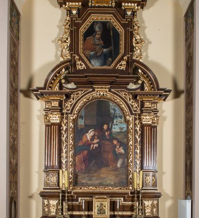 Zdjęcie nr 1: Ołtarz architektoniczny, jednokondygnacyjny, jednoosiowy, ze zwieńczeniem. Ołtarz prostopadłościenny z drewnianą mensą i drewnianym antepedium artykułowanym trzema prostokątnymi płycinami. Retabulum osadzone na nieznacznie zryzalitowanym cokole, lekko wstępującym pośrodku w kolejną partię retabulum. Część środkową ołtarza ujmuje para filarów o czworobocznym przekroju, ustawionych na tle pilastrów, osadzonych na wysokich cokołach i podtrzymujących przerwane belkowanie ze wspartym na nim przerwanym, półkolistym przyczółkiem. Część środkowa belkowania jest wyniesiona nieco wyżej. Pole części środkowej retabulum  ma kształt stojącego prostokąta zamkniętego półkolistym łukiem nadwieszonym. Osadzone na wyłamującym się pośrodku gzymsie zwieńczenie ma postać stojącego prostokąta wypełnionego płyciną z uszakami w narożach, zamkniętą trójbocznie z ośmioboku. Pole środkowe w formie wydłużonego ośmioboku. Zwieńczenie domyka szczyt z formie przerwanego, trójkątnego przyczółka usytuowanego na przerwanym belkowaniu. Środkową płycinę antepedium zdobi płaskorzeźbiony monogram SJ na tle narzędzi ciesielskich (?), boczne ornamentyka roślinna. W partiach cokołu retabulum, cokołów filarów, fryzu oraz górnych naroży części środkowej nastawy są motywy stylizowanej dekoracji roślinnej. Obramienie obrazu głównego ujmuje para wazonów z kwiatami lilii, natomiast boki zwieńczenia ołtarza para ażurowych, akantowych uszaków. W szczycie, po bokach, na przerwanym przyczółku jest para płonących wazonów, pośrodku natomiast kartusz z napisem: „ITE AD JOSEPH” oraz krzyż zdobiony wicią winnej latorośli. W polu części środkowej znajduje się przedstawienie „Pokłonu pasterzy”, w zwieńczeniu natomiast wizerunek św. Stanisława biskupa. Struktura retabulum utrzymana jest w kolorystyce pokostowanego drewna, partie detalu architektonicznego i ornamentyka są złocone. Na mensie napis „MEMENTO - FUNDATORIS / JOSEPHI".  