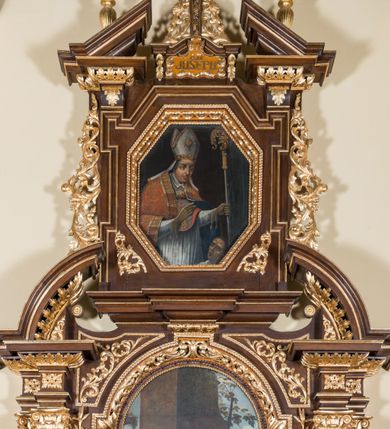 Zdjęcie nr 2: Ołtarz architektoniczny, jednokondygnacyjny, jednoosiowy, ze zwieńczeniem. Ołtarz prostopadłościenny z drewnianą mensą i drewnianym antepedium artykułowanym trzema prostokątnymi płycinami. Retabulum osadzone na nieznacznie zryzalitowanym cokole, lekko wstępującym pośrodku w kolejną partię retabulum. Część środkową ołtarza ujmuje para filarów o czworobocznym przekroju, ustawionych na tle pilastrów, osadzonych na wysokich cokołach i podtrzymujących przerwane belkowanie ze wspartym na nim przerwanym, półkolistym przyczółkiem. Część środkowa belkowania jest wyniesiona nieco wyżej. Pole części środkowej retabulum  ma kształt stojącego prostokąta zamkniętego półkolistym łukiem nadwieszonym. Osadzone na wyłamującym się pośrodku gzymsie zwieńczenie ma postać stojącego prostokąta wypełnionego płyciną z uszakami w narożach, zamkniętą trójbocznie z ośmioboku. Pole środkowe w formie wydłużonego ośmioboku. Zwieńczenie domyka szczyt z formie przerwanego, trójkątnego przyczółka usytuowanego na przerwanym belkowaniu. Środkową płycinę antepedium zdobi płaskorzeźbiony monogram SJ na tle narzędzi ciesielskich (?), boczne ornamentyka roślinna. W partiach cokołu retabulum, cokołów filarów, fryzu oraz górnych naroży części środkowej nastawy są motywy stylizowanej dekoracji roślinnej. Obramienie obrazu głównego ujmuje para wazonów z kwiatami lilii, natomiast boki zwieńczenia ołtarza para ażurowych, akantowych uszaków. W szczycie, po bokach, na przerwanym przyczółku jest para płonących wazonów, pośrodku natomiast kartusz z napisem: „ITE AD JOSEPH” oraz krzyż zdobiony wicią winnej latorośli. W polu części środkowej znajduje się przedstawienie „Pokłonu pasterzy”, w zwieńczeniu natomiast wizerunek św. Stanisława biskupa. Struktura retabulum utrzymana jest w kolorystyce pokostowanego drewna, partie detalu architektonicznego i ornamentyka są złocone. Na mensie napis „MEMENTO - FUNDATORIS / JOSEPHI".  