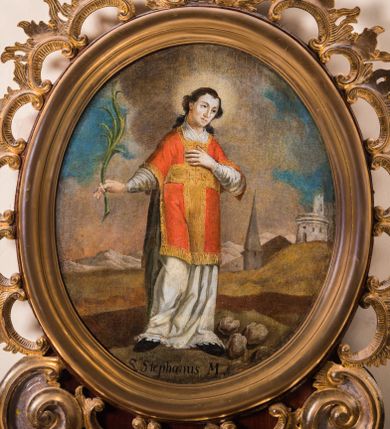 Zdjęcie nr 1: Obraz w kształcie stojącego owalu przedstawia całopostaciowy wizerunek św. Szczepana stojącego w kontrapoście i zwróconego w trzech czwartych w lewo. Przechyloną głowę charakteryzuje owalna twarz o młodzieńczych, pozbawionych zarostu rysach oraz długie, falowane, opadające na plecy włosy. Święty ubrany jest w albę i czerwoną dalmatykę ze złoconymi obszyciami i pretekstą w formie krzyża. Lewą rękę wspiera na piersiach, w prawej wysuniętej w bok trzyma gałązkę palmową. Głowę świętego okala świetlisty nimb, u jego stóp, po prawej stronie leżą trzy kamienie. Święty Szczepan ukazany jest na tle górzystego pejzażu o obniżonej linii horyzontu, z elementami architektury po prawej stronie kompozycji, gdzie wyróżnia się strzelista wieża kościoła. Znaczną część tła zajmuje partia pokrytego obłokami nieba. W dolnej części obrazu znajduje się napis „S(anctus) Stephanus M(artyr)”.       
Obraz ujęty jest rzeźbioną, ażurową ramą z motywem rocaille’u, parą wolut po bokach u dołu oraz motywem kartusza w zwieńczeniu. Całość osadzona jest wtórnie na sarkofagowym ołtarzu w formie niewielkiej konsoli.   