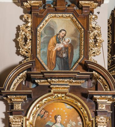Zdjęcie nr 5: Ołtarz architektoniczny, jednokondygnacyjny, jednoosiowy, ze zwieńczeniem. Ołtarz prostopadłościenny z drewnianą mensą i drewnianym antepedium artykułowanym trzema prostokątnymi płycinami. Retabulum osadzone na lekko zryzalitowanym cokole, lekko wstępującym pośrodku w kolejną partię retabulum. Część środkową ołtarza ujmuje para filarów o czworobocznym przekroju, osadzonych na wysokich cokołach i podtrzymujących przerwane belkowanie ze wspartym na nim przerwanym, półkolistym przyczółkiem. Część środkowa belkowania jest wyniesiona nieco wyżej. Pole części środkowej ma kształt stojącego prostokąta zamkniętego półkolistym łukiem nadwieszonym. Osadzone na wyłamującym się pośrodku gzymsie zwieńczenie jest w formie stojącego prostokąta wypełnionego płyciną z uszakami w narożach, zamkniętą trapezoidalnym łukiem. Pole środkowe ma postać wydłużonego ośmioboku. Zwieńczenie zamyka szczyt w formie przerwanego, trójkątnego przyczółka osadzonego na przerwanym belkowaniu. Partie fryzu retabulum zdobi motyw prostokątnych rozet. Boki zwieńczenia zdobi para ażurowych, ornamentalnych uszaków. W szczycie, pośrodku, na niewielkim cokoliku znajduje się monogram maryjny dołem ujęty bukietem kwiatów, górą koroną. W polu części środkowej umieszczono obraz Matki Boskiej Niepokalanie Poczętej, na zasuwie wizerunek Matki Boskiej Bolesnej. W zwieńczeniu jest przedstawienie św. Józefa. Struktura retabulum utrzymana jest w kolorystyce pokostowanego drewna, partie detalu architektonicznego i ornamentyka są złocone.   

