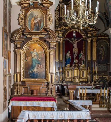 Zdjęcie nr 6: Ołtarz architektoniczny, jednokondygnacyjny, jednoosiowy, ze zwieńczeniem. Ołtarz prostopadłościenny z drewnianą mensą i drewnianym antepedium artykułowanym trzema prostokątnymi płycinami. Retabulum osadzone na lekko zryzalitowanym cokole, lekko wstępującym pośrodku w kolejną partię retabulum. Część środkową ołtarza ujmuje para filarów o czworobocznym przekroju, osadzonych na wysokich cokołach i podtrzymujących przerwane belkowanie ze wspartym na nim przerwanym, półkolistym przyczółkiem. Część środkowa belkowania jest wyniesiona nieco wyżej. Pole części środkowej ma kształt stojącego prostokąta zamkniętego półkolistym łukiem nadwieszonym. Osadzone na wyłamującym się pośrodku gzymsie zwieńczenie jest w formie stojącego prostokąta wypełnionego płyciną z uszakami w narożach, zamkniętą trapezoidalnym łukiem. Pole środkowe ma postać wydłużonego ośmioboku. Zwieńczenie zamyka szczyt w formie przerwanego, trójkątnego przyczółka osadzonego na przerwanym belkowaniu. Partie fryzu retabulum zdobi motyw prostokątnych rozet. Boki zwieńczenia zdobi para ażurowych, ornamentalnych uszaków. W szczycie, pośrodku, na niewielkim cokoliku znajduje się monogram maryjny dołem ujęty bukietem kwiatów, górą koroną. W polu części środkowej umieszczono obraz Matki Boskiej Niepokalanie Poczętej, na zasuwie wizerunek Matki Boskiej Bolesnej. W zwieńczeniu jest przedstawienie św. Józefa. Struktura retabulum utrzymana jest w kolorystyce pokostowanego drewna, partie detalu architektonicznego i ornamentyka są złocone.   

