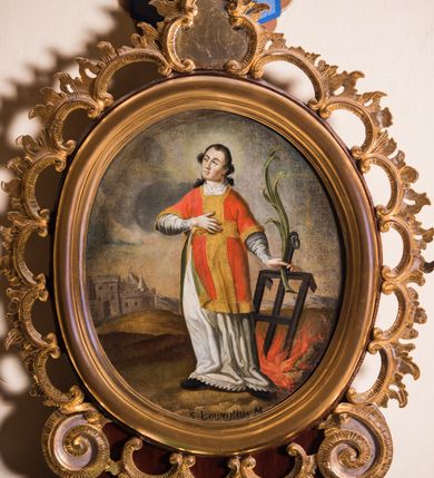 Zdjęcie nr 2: Obraz w kształcie stojącego owalu przedstawia całopostaciowy wizerunek św. Wawrzyńca stojącego w kontrapoście i zwróconego w trzech czwartych w prawo. Przechyloną nieznacznie głowę charakteryzuje pociągła twarz o wyrazistych, młodzieńczych, pozbawionych zarostu rysach oraz długie, falowane, opadające na plecy włosy o wydatnych kępkach na wysokości uszu. Święty ubrany jest w albę i czerwoną dalmatykę ze złoconymi obszyciami i pretekstą w formie krzyża. Prawą rękę wspiera na piersiach, w lewej, wysuniętej w bok trzyma gałązkę palmową i kratę paleniskową wetkniętą w płonące ognisko. Głowę świętego okala jasny, świetlisty nimb. Święty Wawrzyniec ukazany jest na tle górzystego pejzażu o obniżonej linii horyzontu, z elementami architektury otoczonego murem miasta po lewej stronie kompozycji. Znaczną część tła zajmuje partia pokrytego obłokami nieba. W dolnej części obrazu znajduje się napis „S(anctus) Laurentius M(artyr)”.  
Obraz ujęty jest rzeźbioną, ażurową ramą z motywem rocaille’u, parą wolut po bokach u dołu oraz motywem kartusza w zwieńczeniu. Całość osadzona jest wtórnie na sarkofagowym ołtarzu w formie niewielkiej konsoli.   

